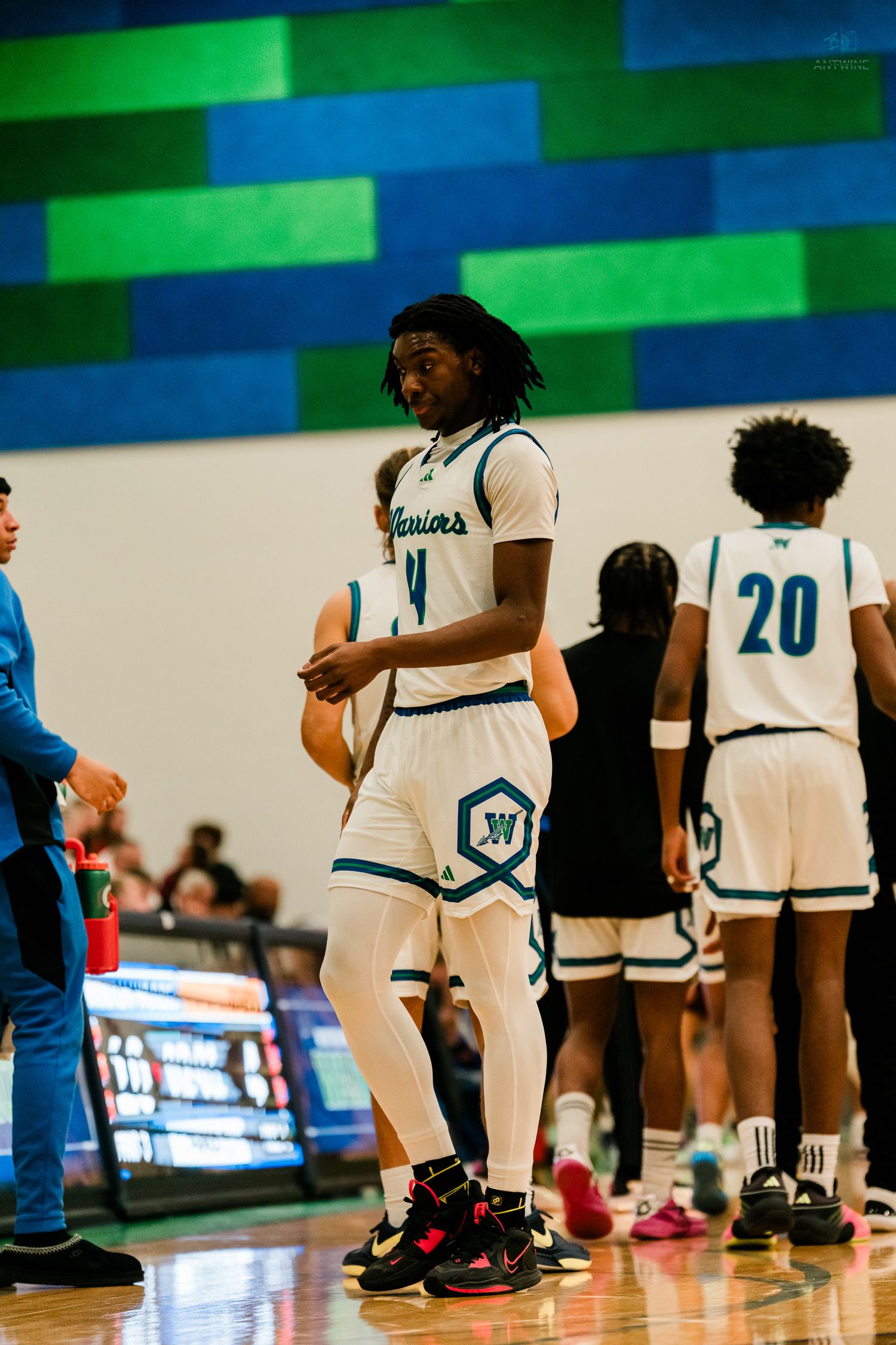 Tall Warriors basketball player #4 in white uniform stands on court during high school basketball game.