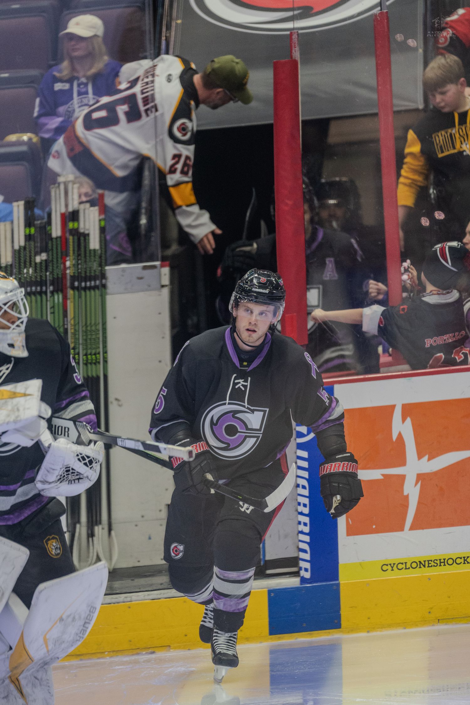 Ice hockey player in black purple C jersey skates onto rink during player introductions at indoor arena.