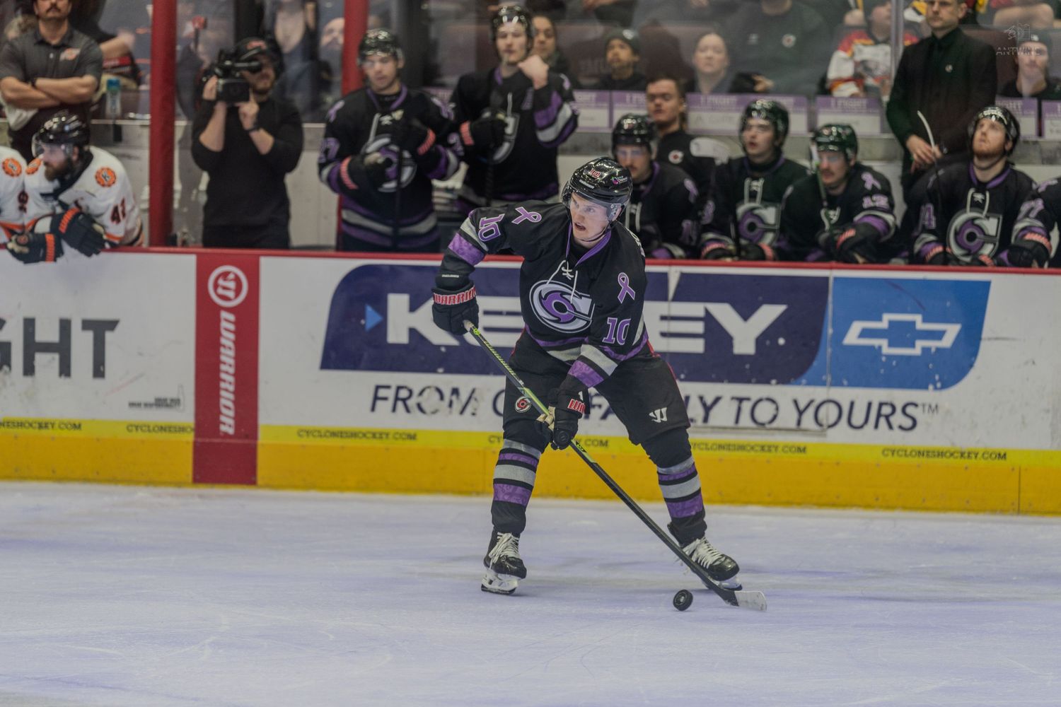 Hockey player in black and purple jersey handles the puck on ice during a professional hockey game.