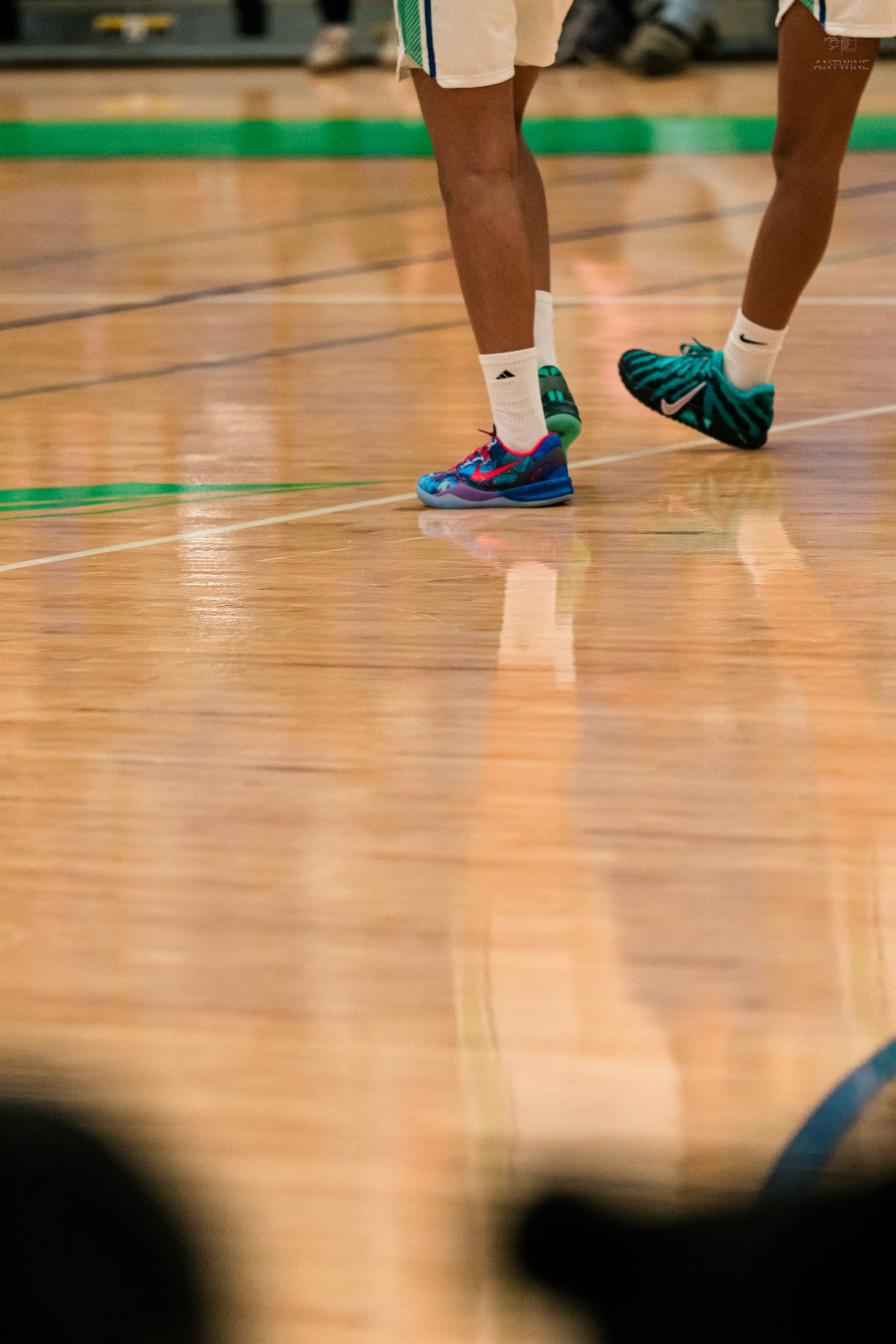 Warriors players wearing colorful Nike and Adidas sneakers walk across a reflective hardwood basketball court.