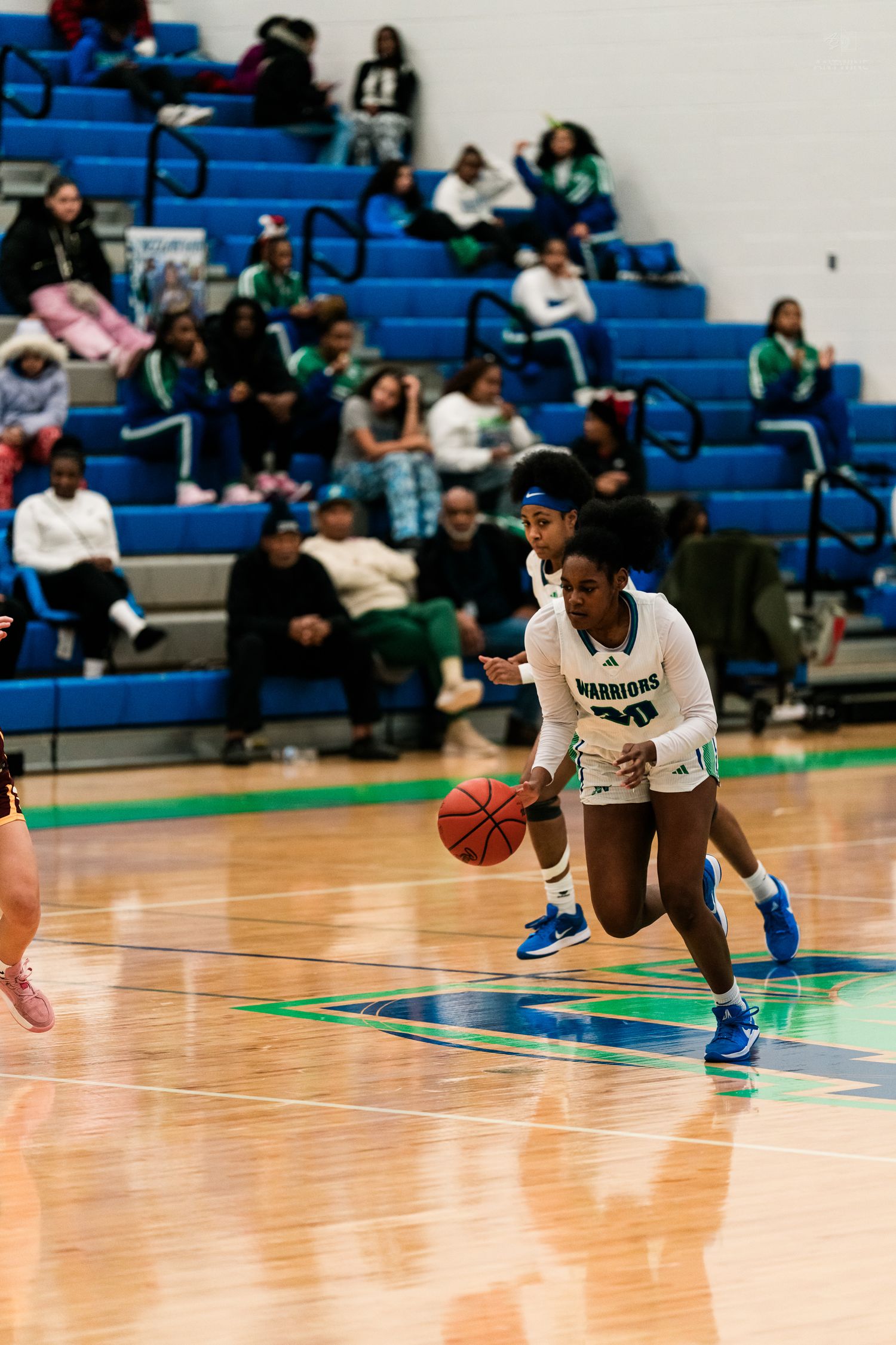 A Warriors girls basketball player in white dribbles the ball low during a high school game.