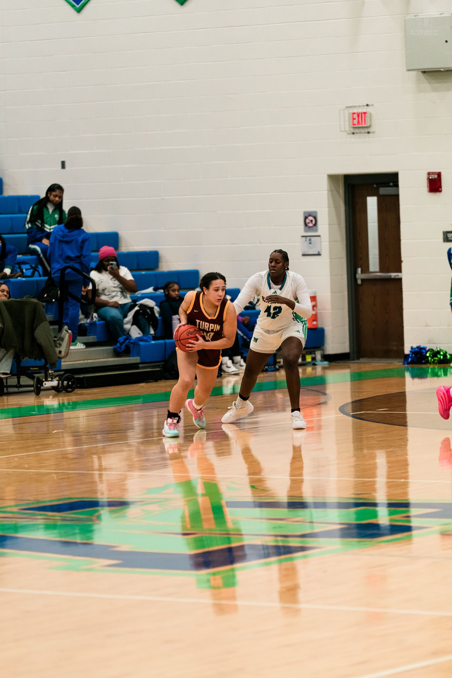 A Turpin girls basketball player dribbles upcourt while a Warriors defender in white jersey number 42 guards her closely.