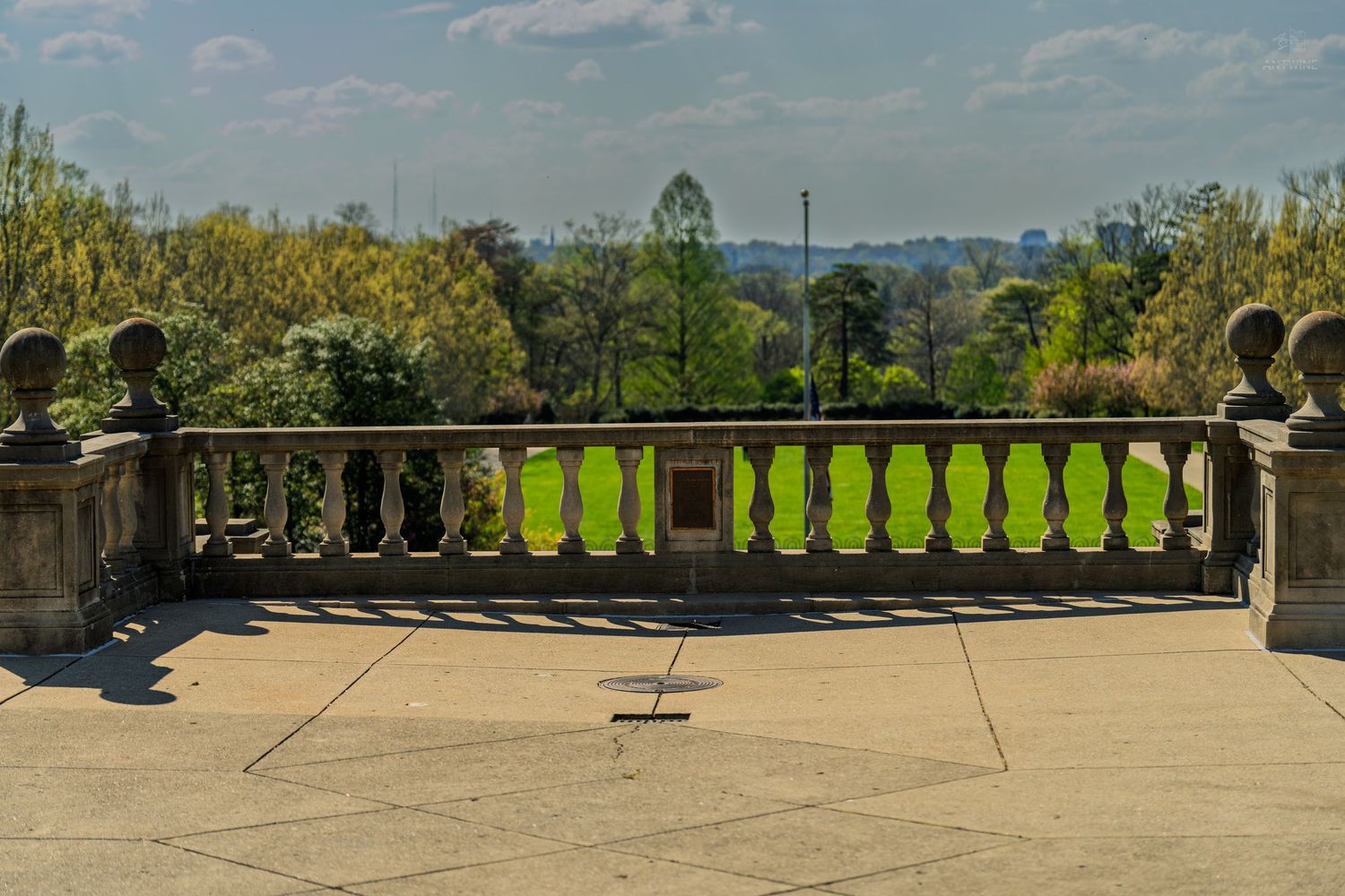 Panoramic view from a classical stone balustrade terrace overlooking lush green lawns and autumn-colored trees.