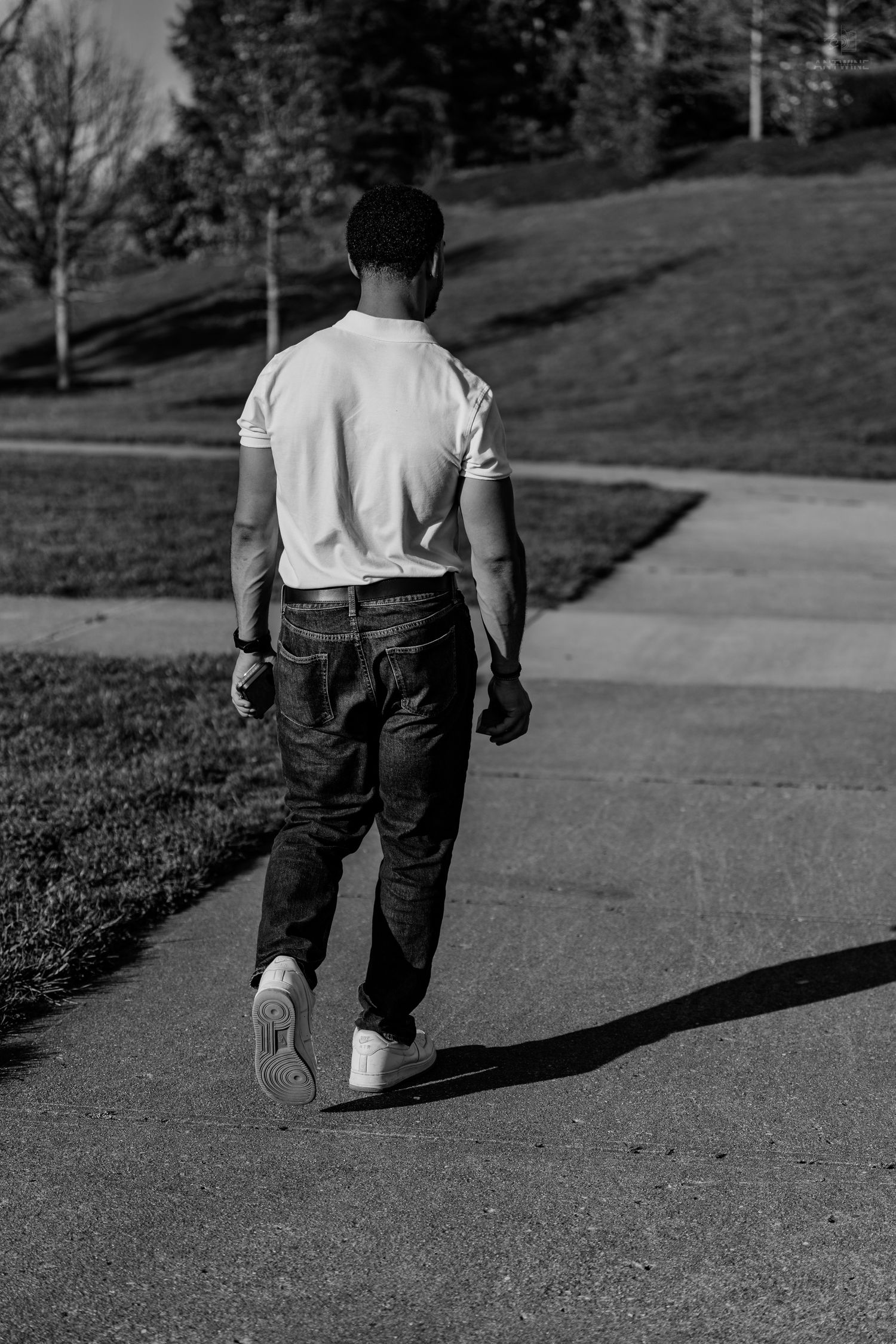 Black and white rear view of a man in a white t-shirt and jeans walking on a path.