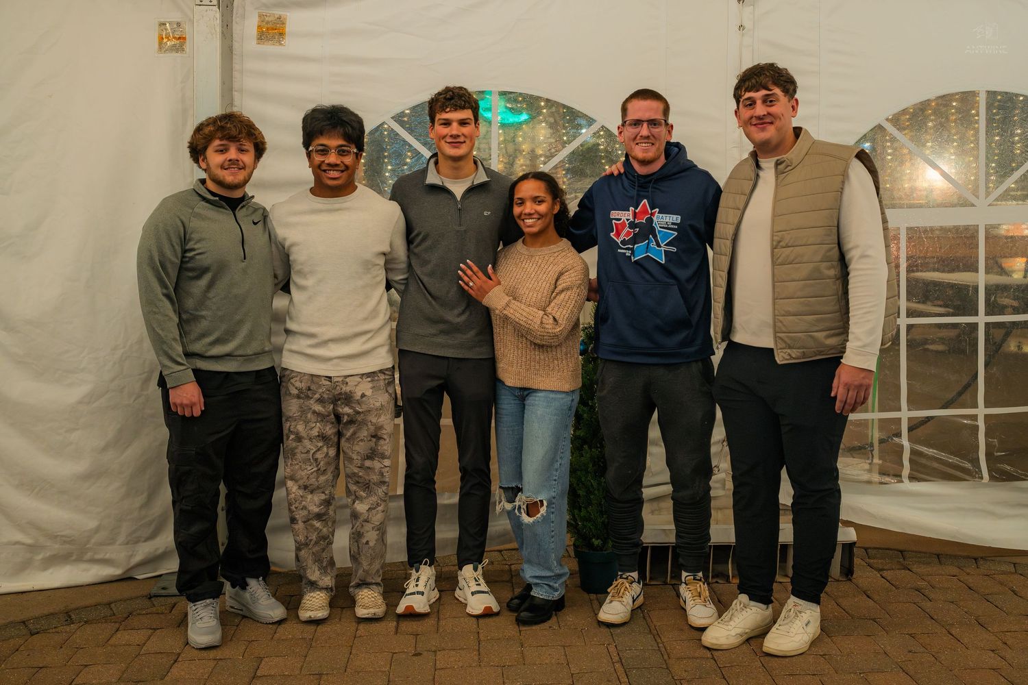 Six friends smile together posing inside a white tent at an event.