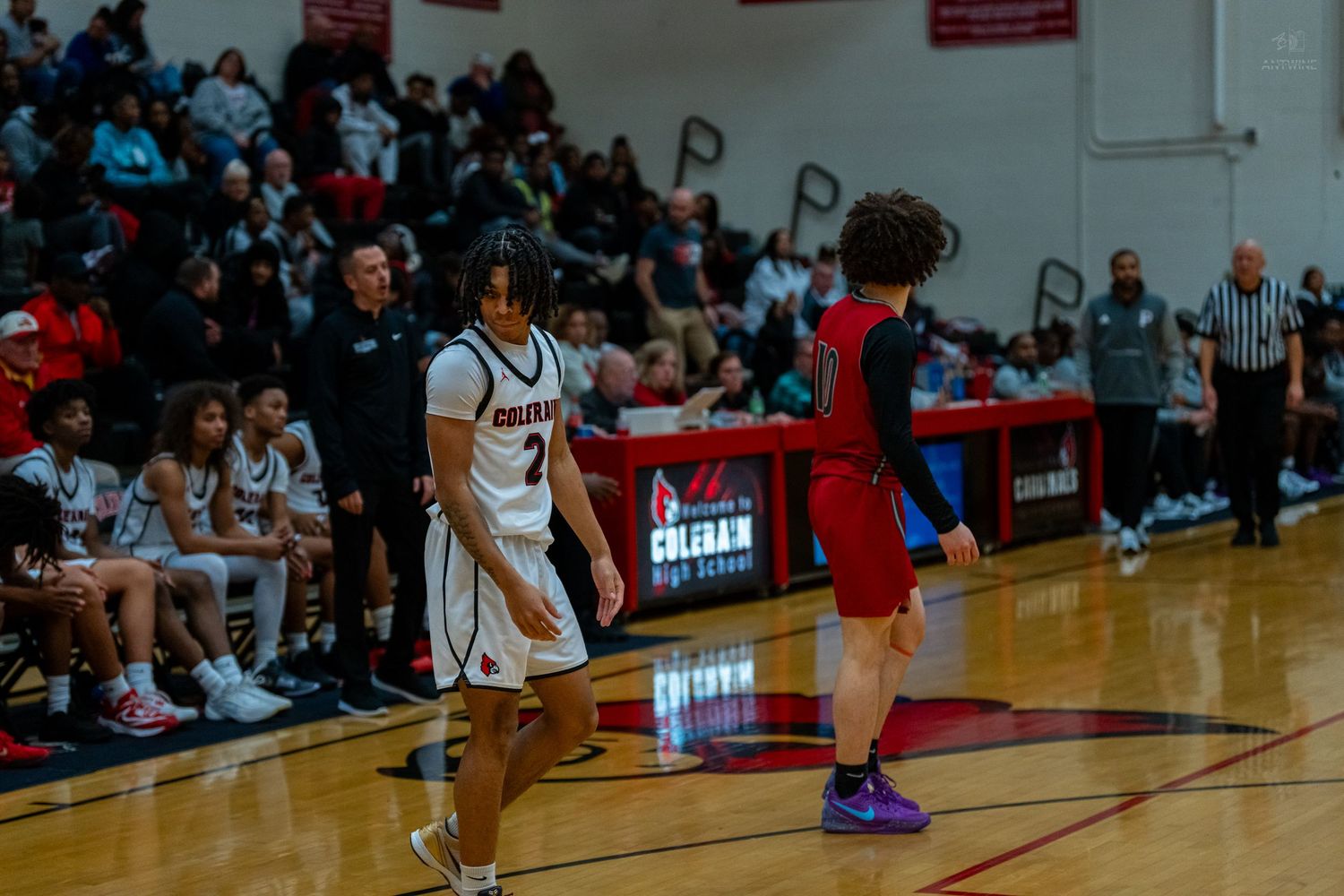 Colerain High School basketball players stand on court during a game with packed stands.