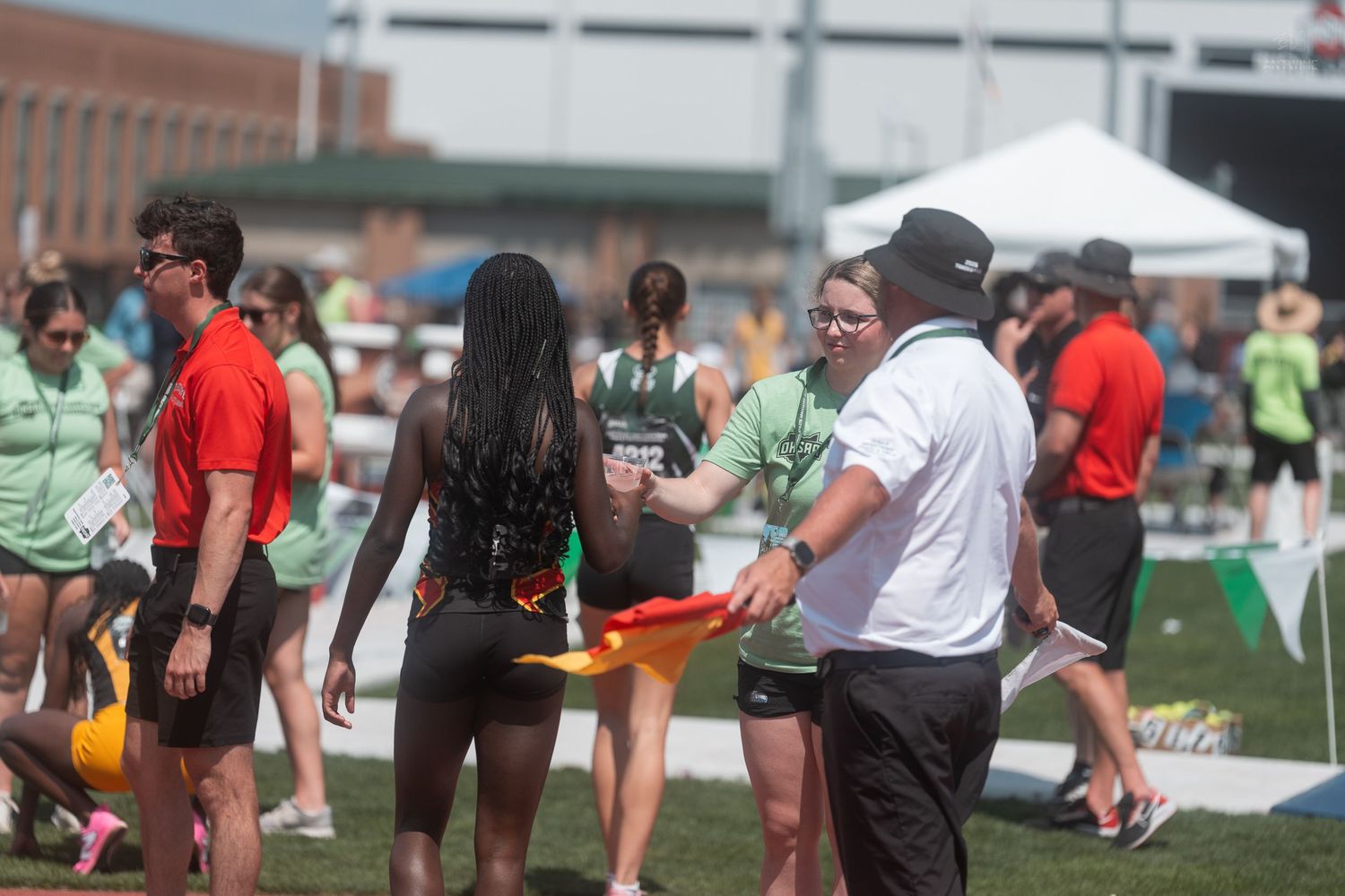 Track and field officials and athletes gather on an infield during a high school track meet.