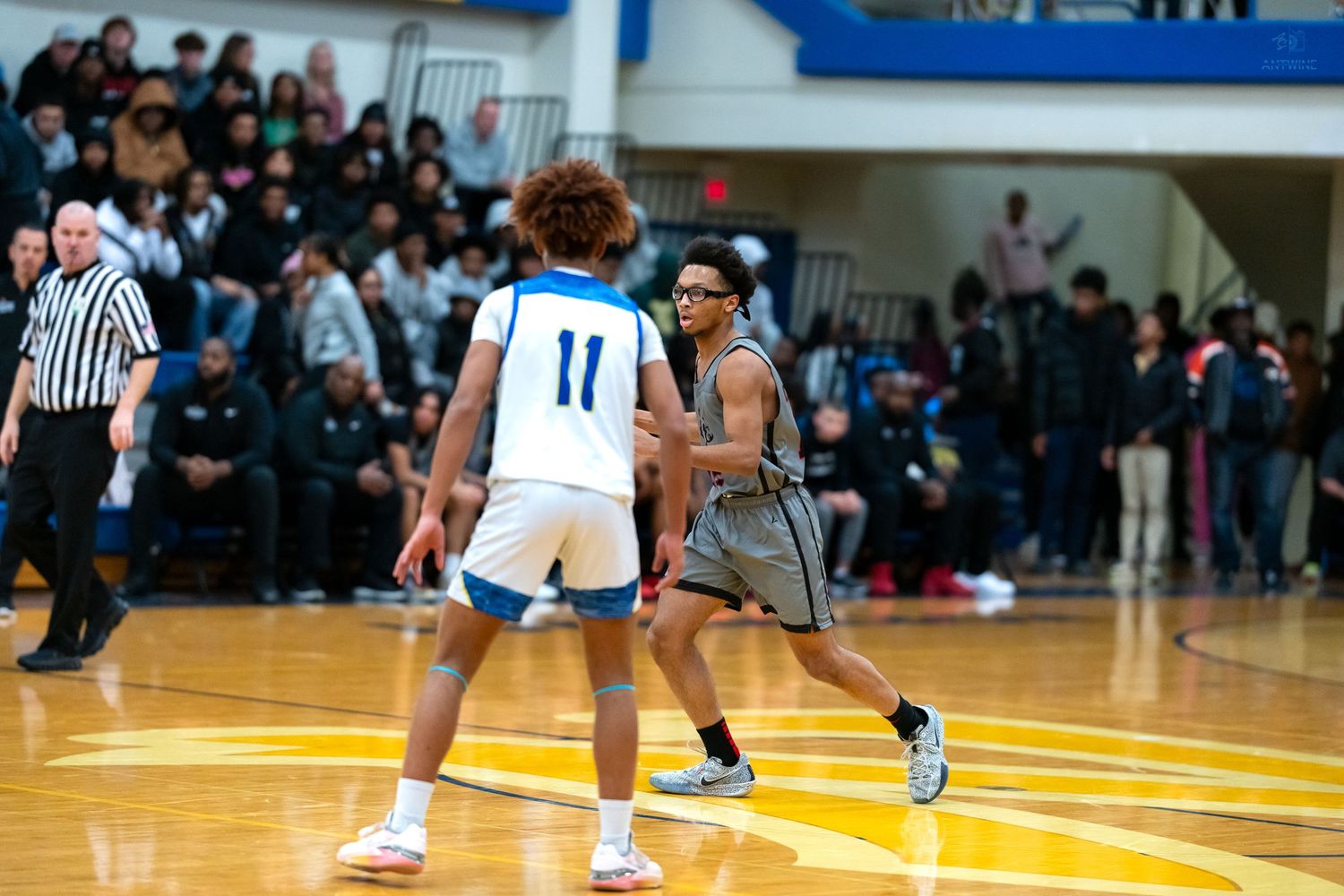 Basketball player wearing number 11 defends against opponent during an indoor high school basketball game.