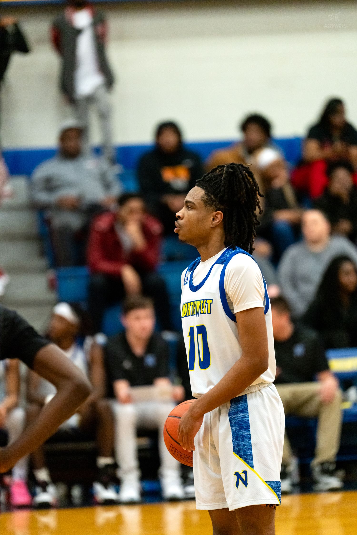 Northwest Knights player number 10 with dreadlocks holds basketball preparing for a free throw in a crowded gymnasium.