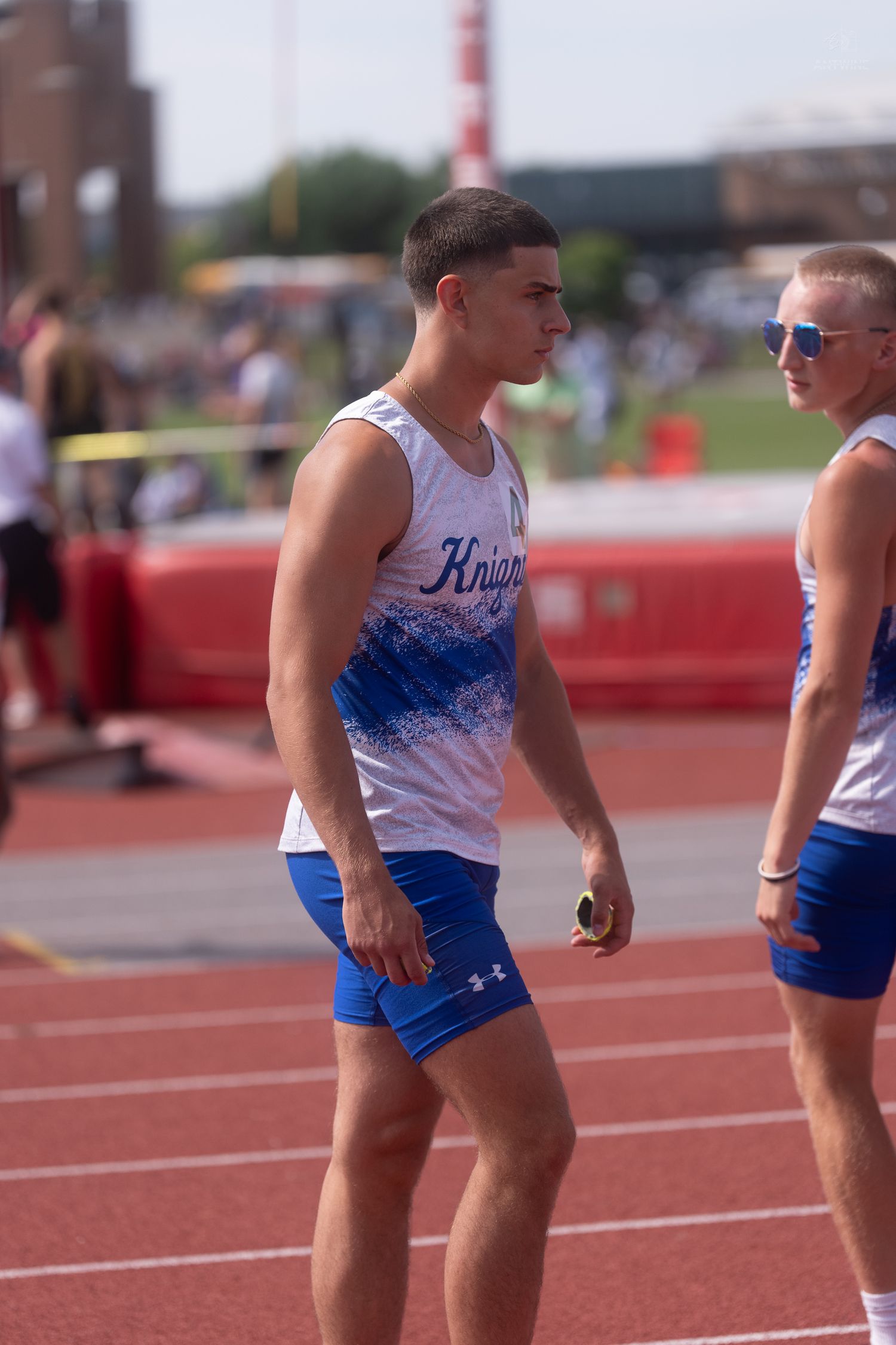 Two male Knights track athletes in blue uniforms prepare for relay race at outdoor competition.
