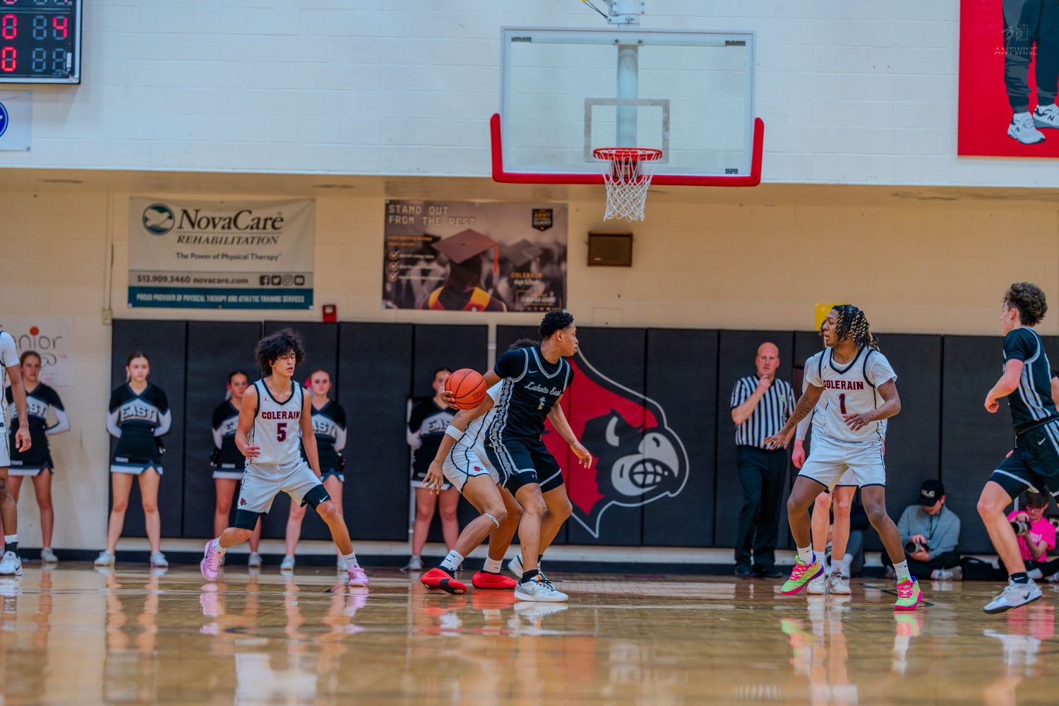 Players compete during a girls high school basketball game on a red and black gymnasium court.