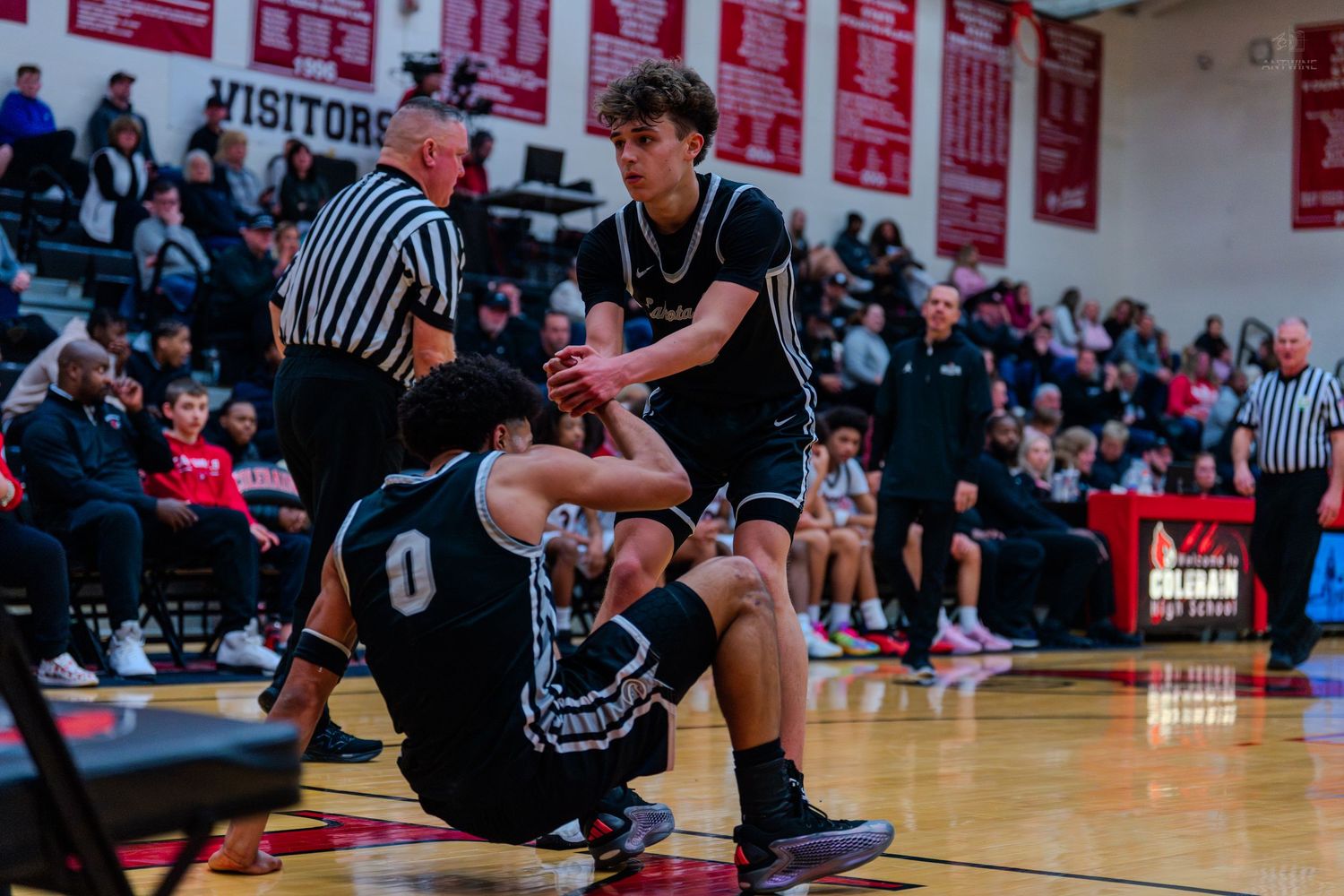 A basketball player helps a fallen teammate off the court during a high school basketball game.