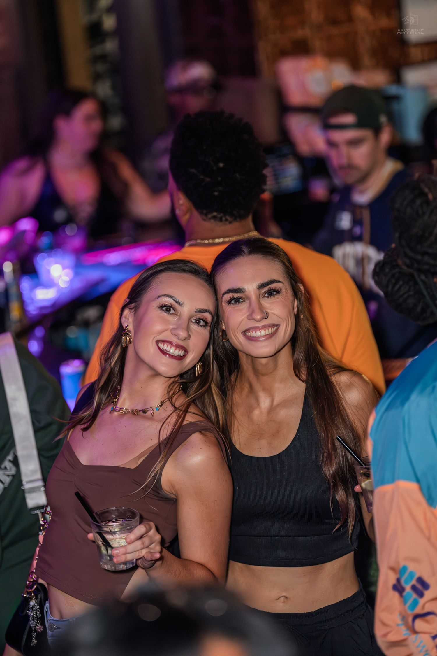 Two smiling women posing together at lively nightclub event.