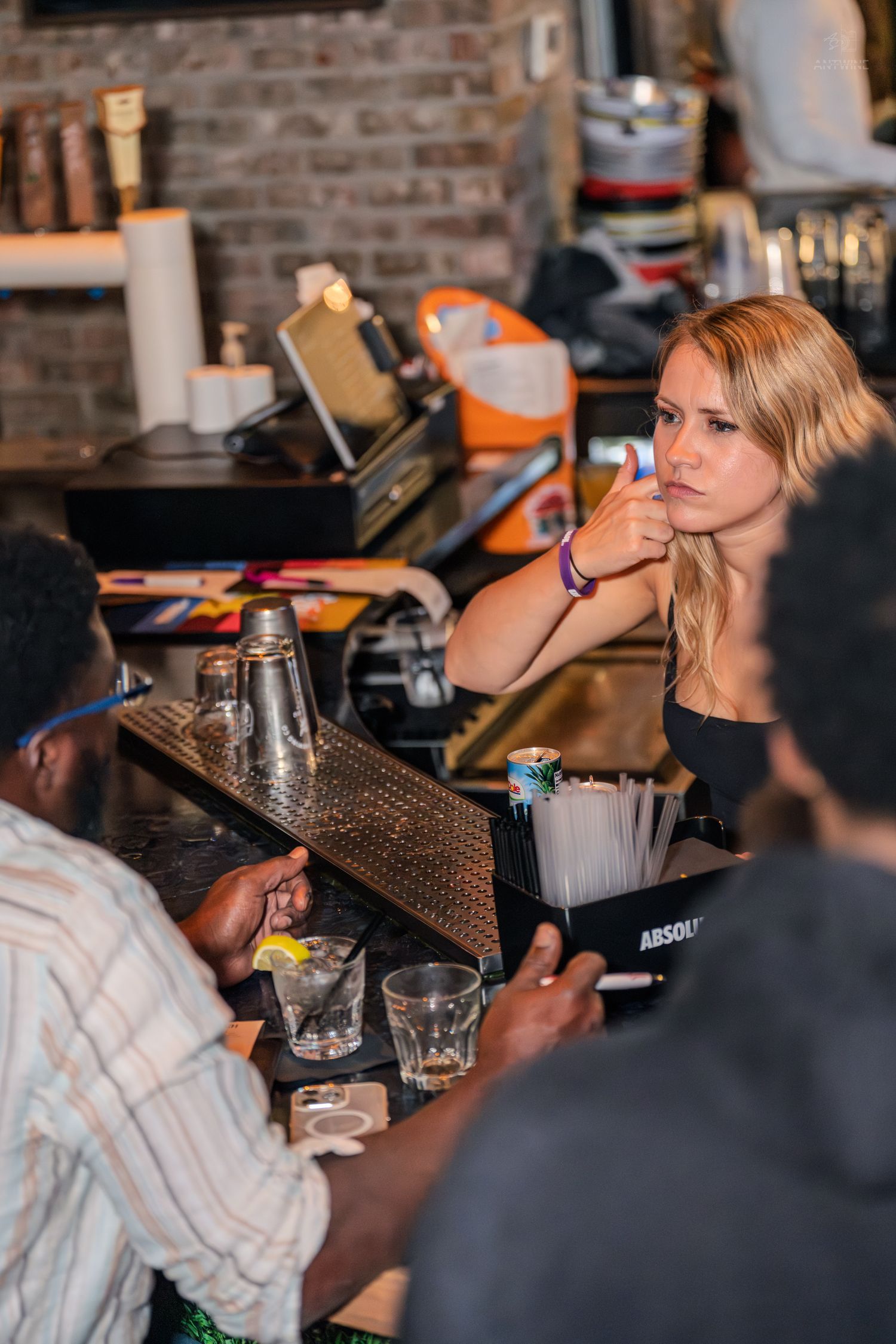 Blonde female bartender serving drinks to customers at a busy bar.