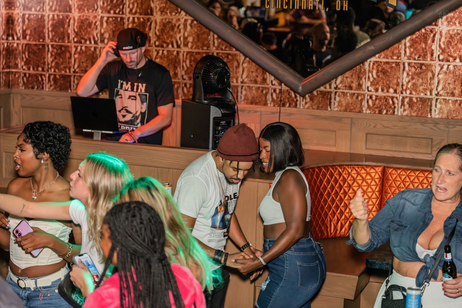 Energetic nightclub crowd dancing while DJ spins music on a colorful dance floor.