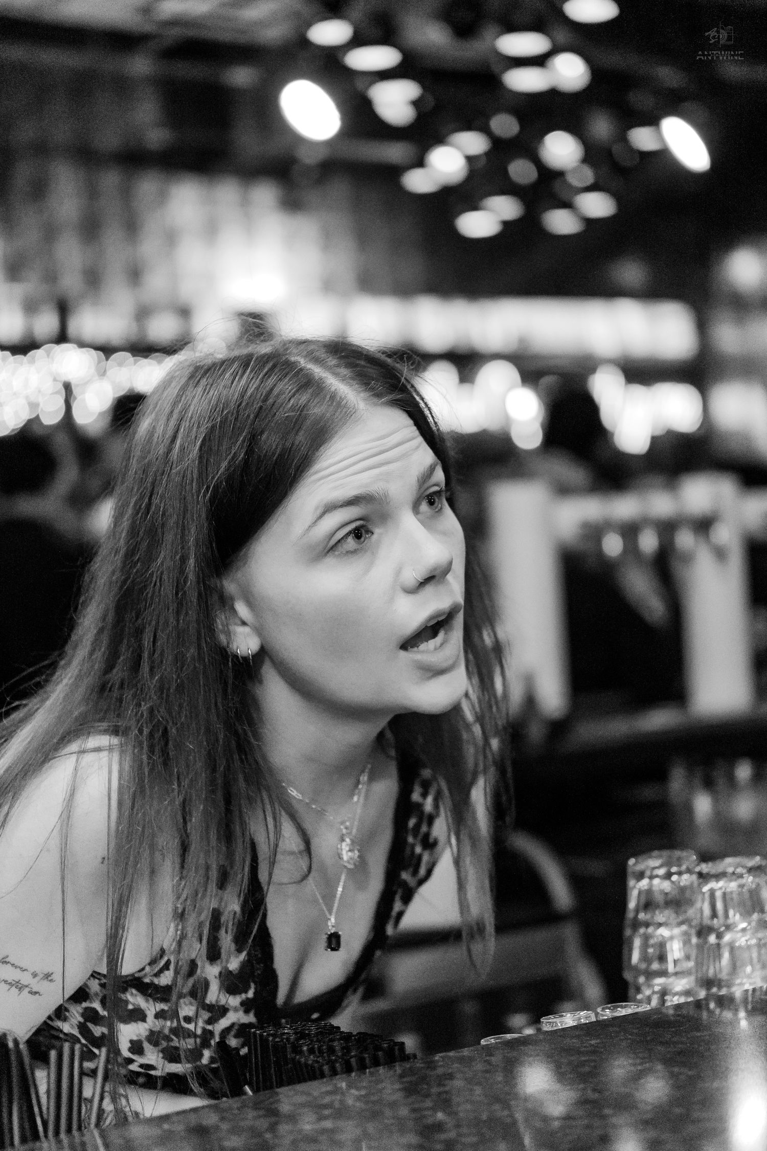 Black and white portrait of a woman with an expressive face sitting at a bar.