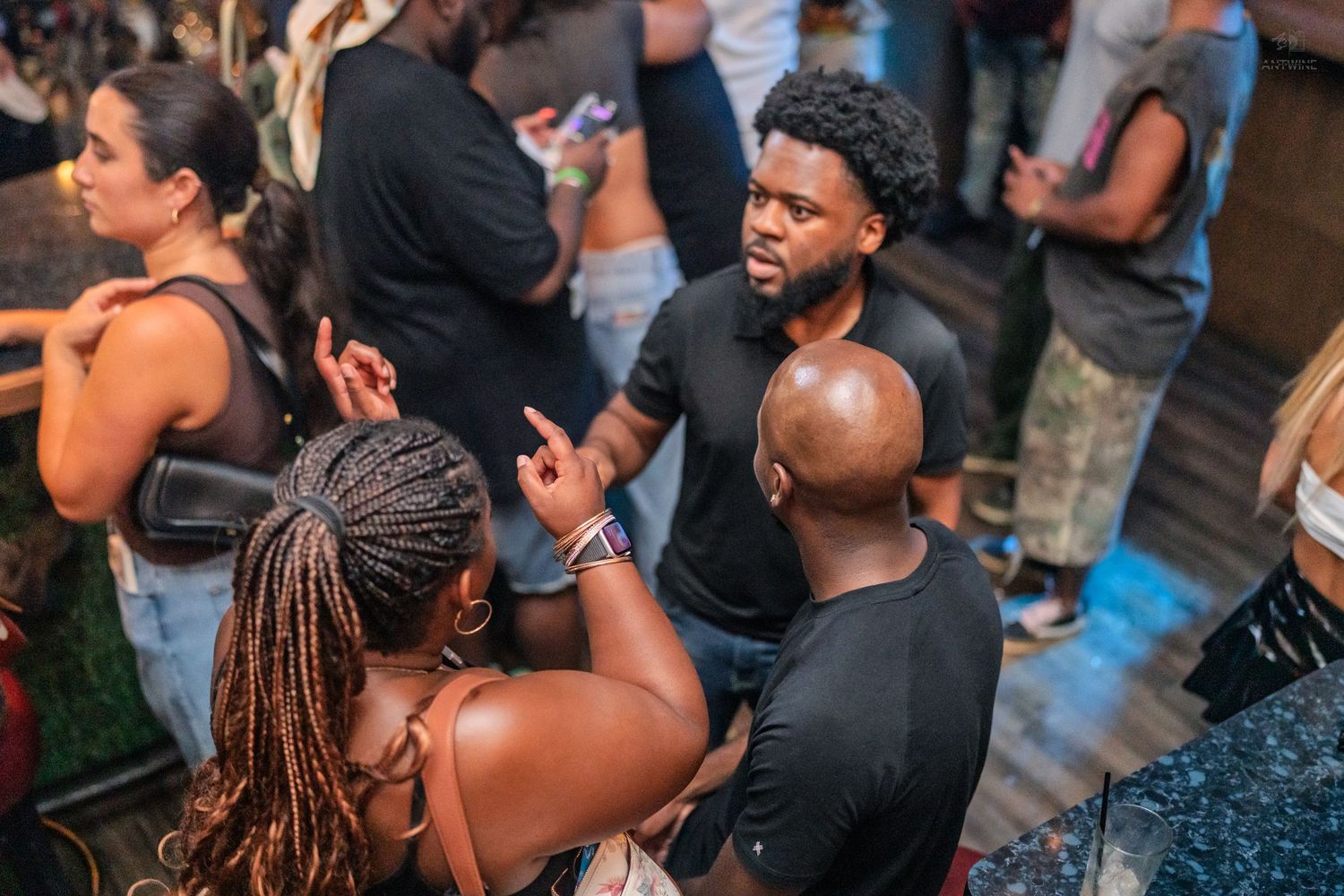 Group of friends conversing and gesturing at a crowded dimly lit nightclub event.