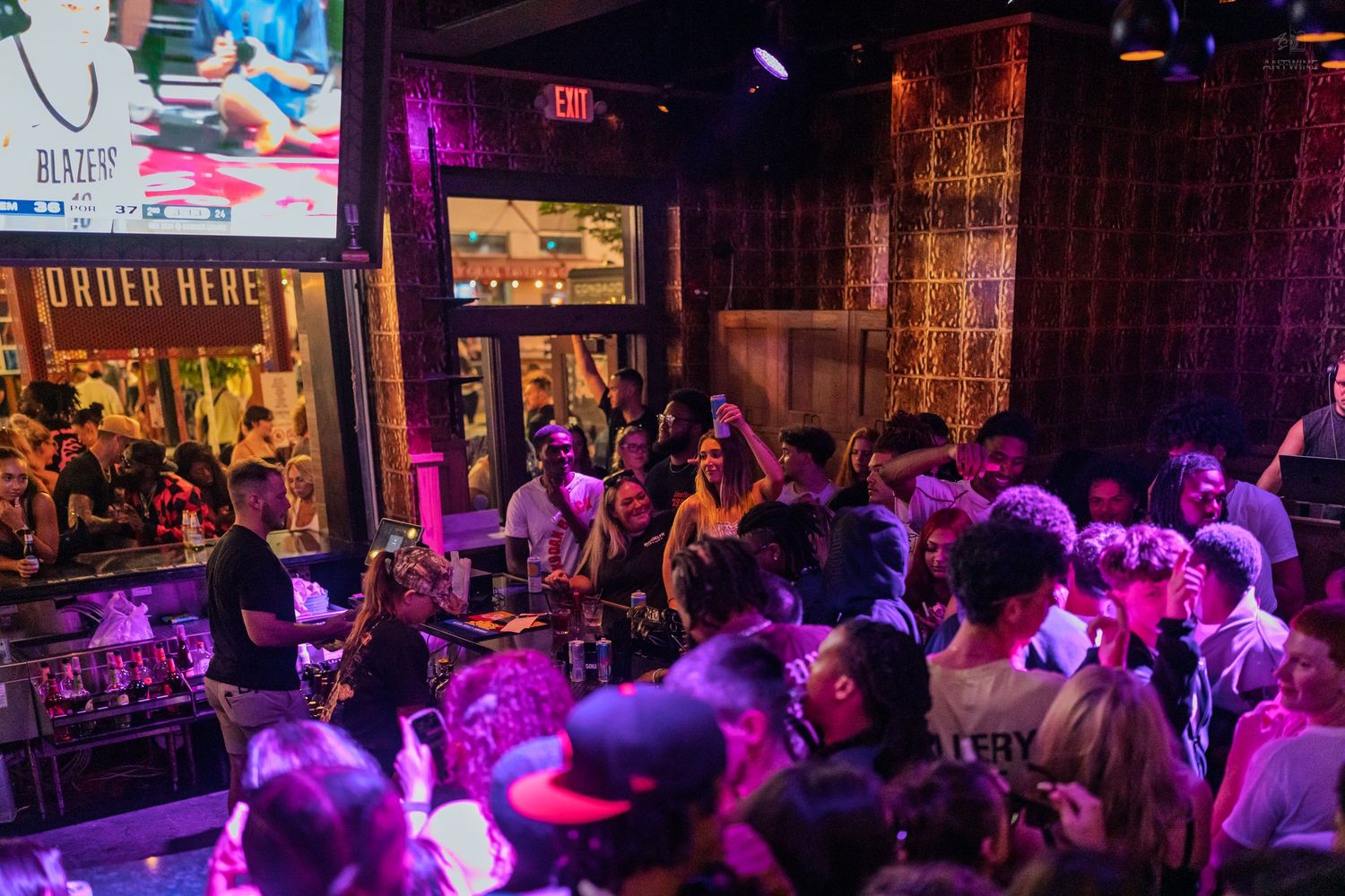 Packed nightclub venue with purple lighting, large screen display, and crowded dance floor near entrance.
