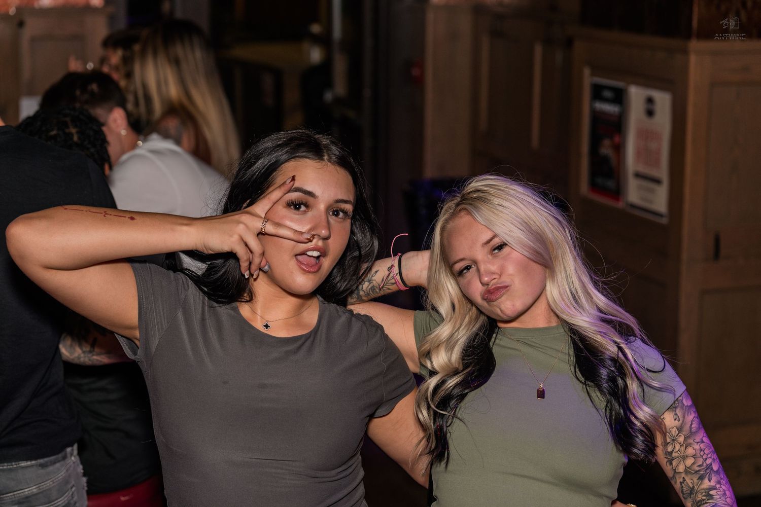 Two young women, brunette and blonde, posing with peace signs at a bar.