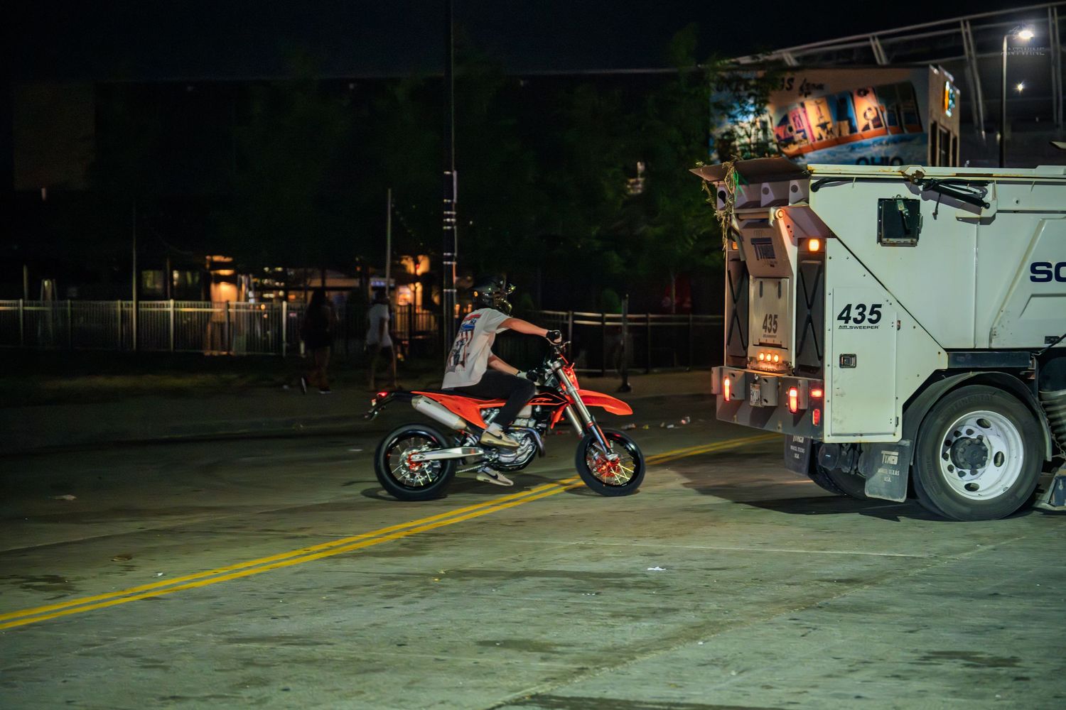 Red dirt bike parked near a decorated truck on a city street at night.