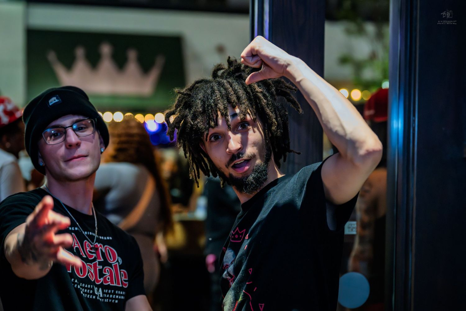 Two young men posing and gesturing near a doorway at a nighttime venue.
