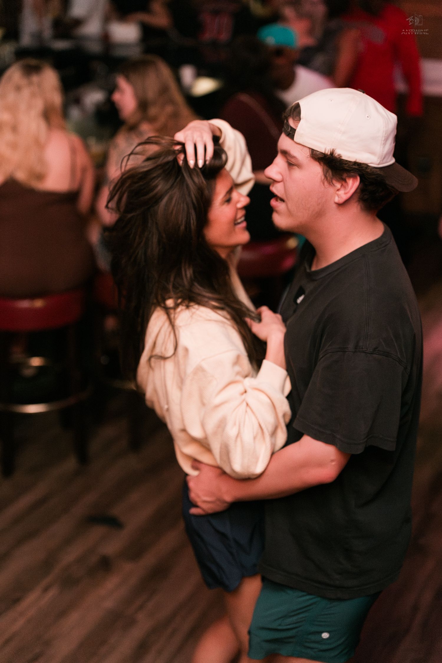 Young couple dancing closely and smiling at each other inside a lively bar setting.