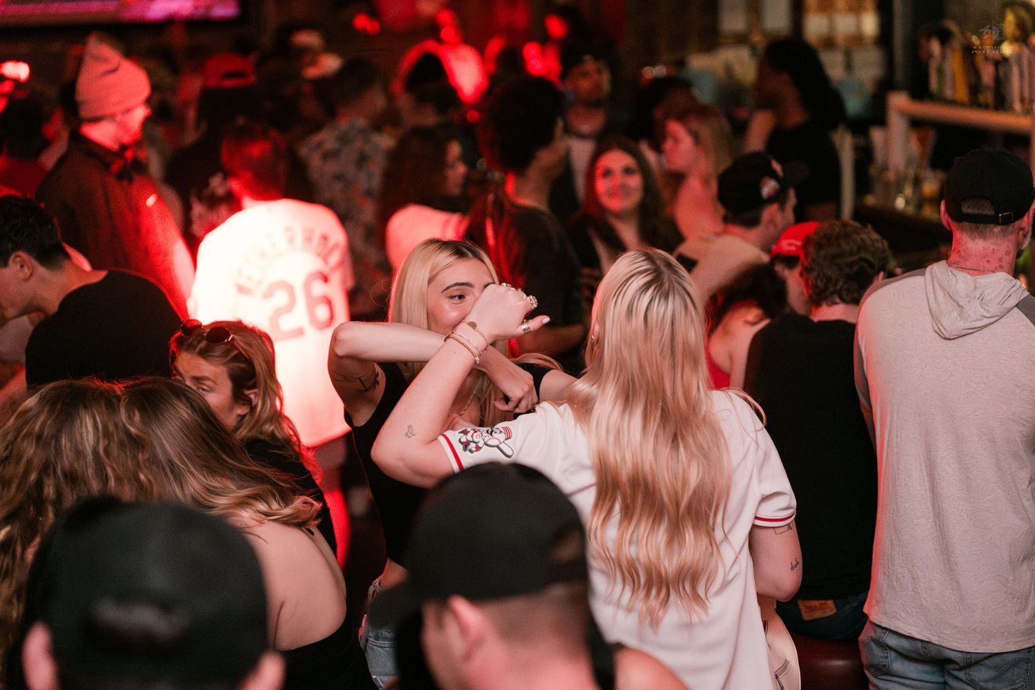 Energetic nightclub crowd dancing under red lights with inflatable props at a bar party.