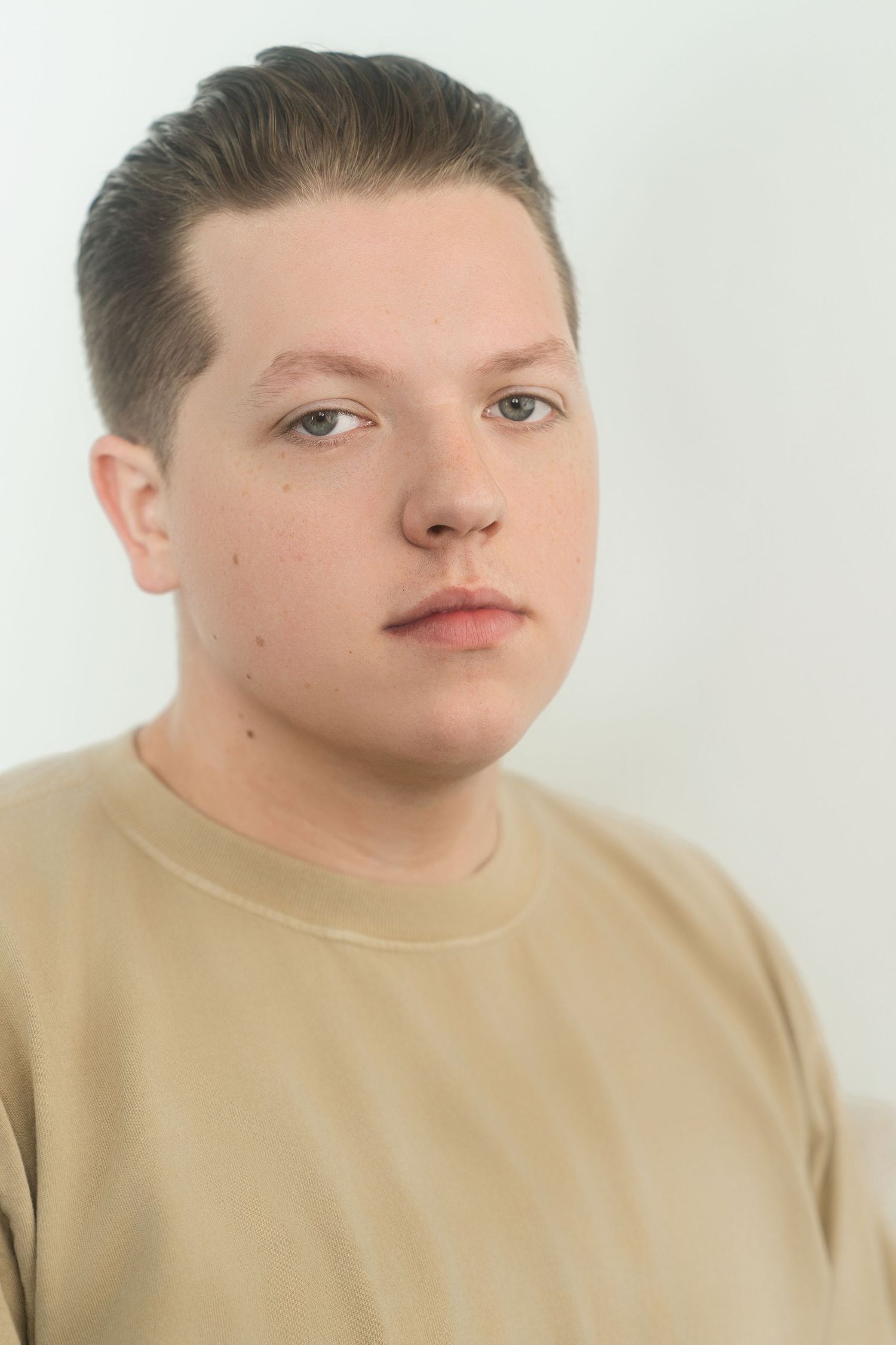 Young man in beige sweatshirt with neutral expression in studio portrait against white background.