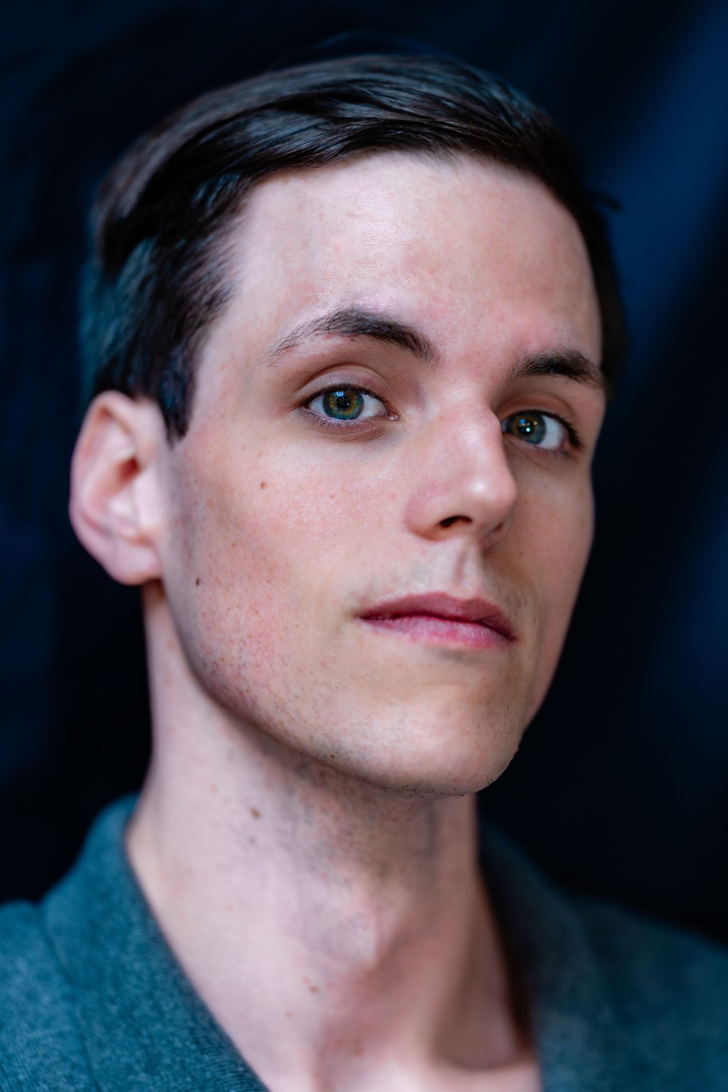 Young man with short dark hair and hazel eyes wearing a teal shirt poses for a professional headshot.
