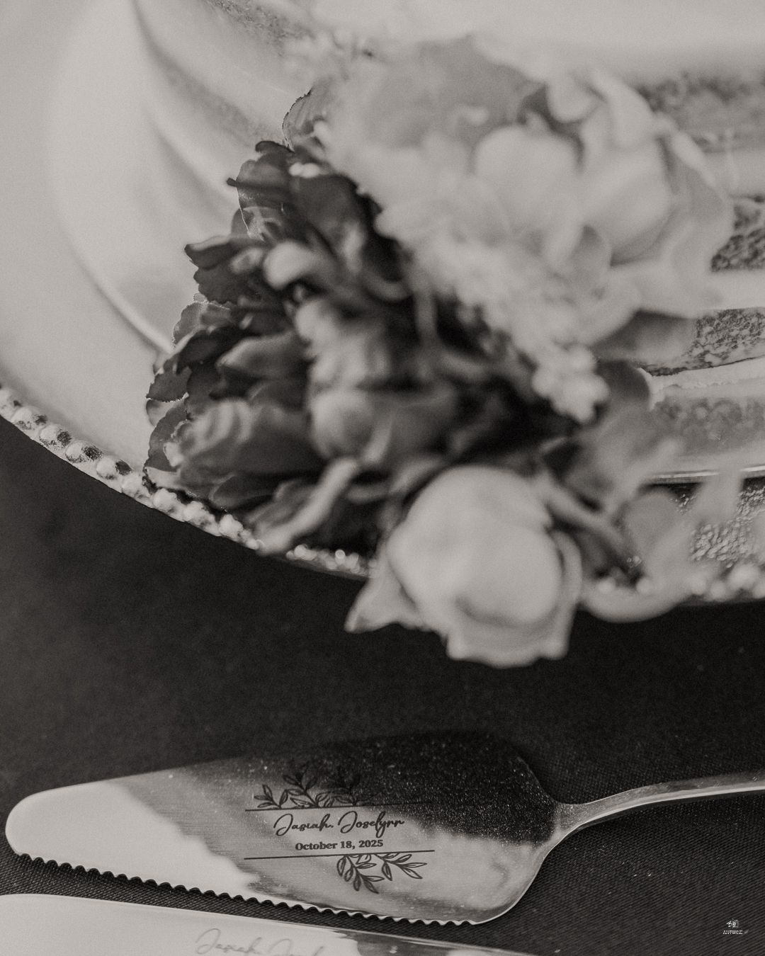Black and white close-up of personalized engraved wedding cake server beside a floral decorated cake.