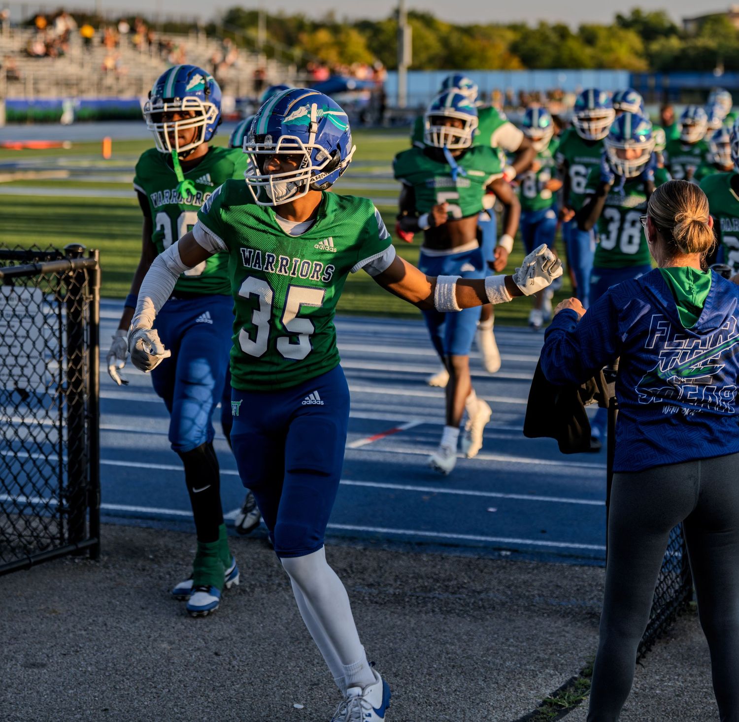 Warriors #35 high-fives fan while leading team onto field before football game.