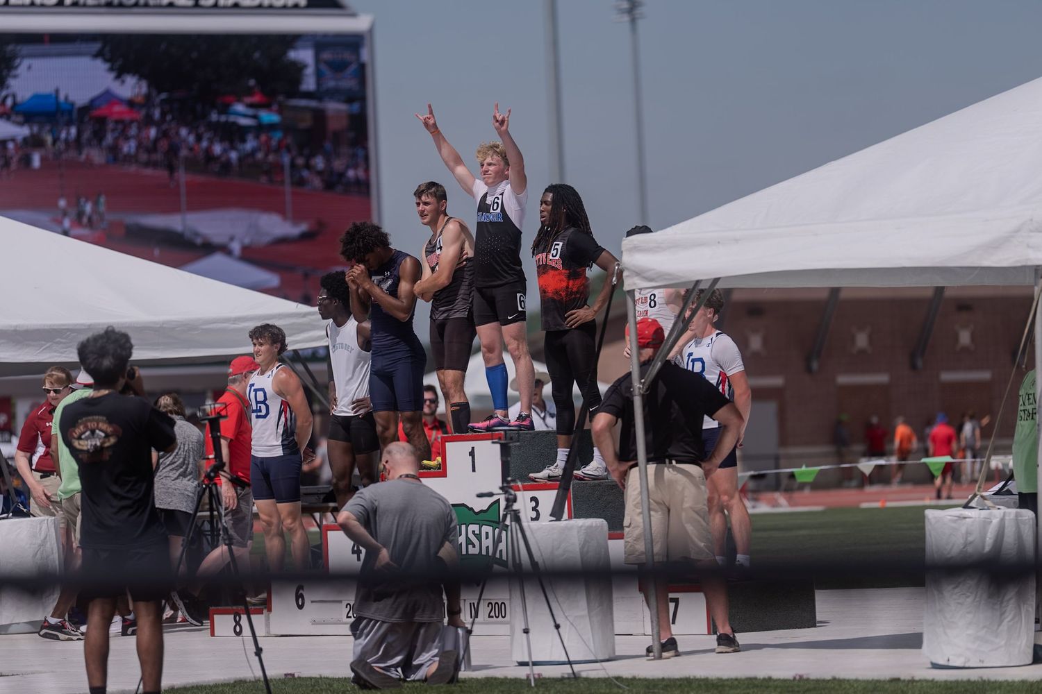 Track and field athletes celebrate on podium at outdoor championship competition.