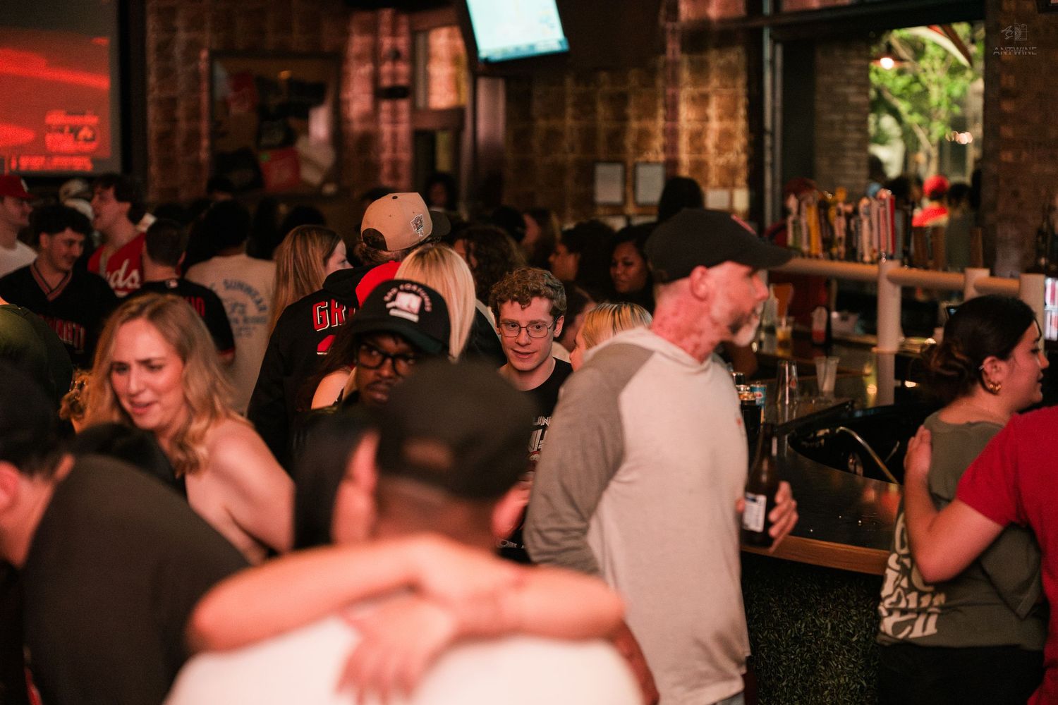 Busy bar scene with diverse crowd of people mingling, laughing, and socializing under warm ambient lighting.