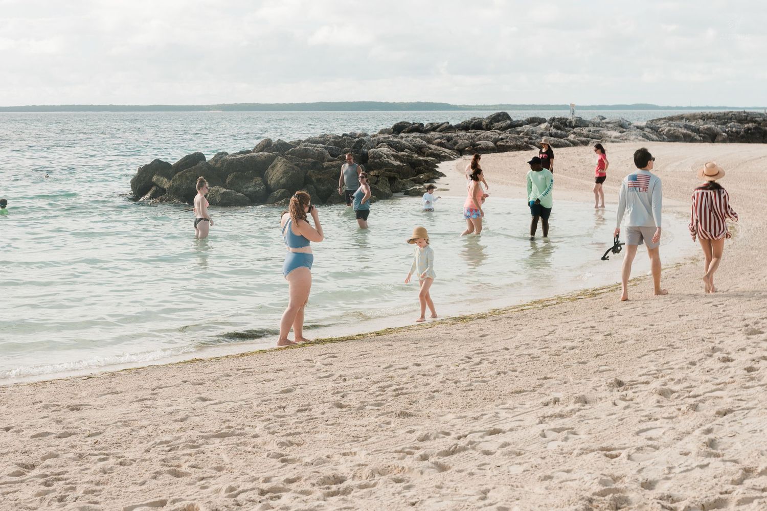 Group of people wading and walking along a scenic rocky shoreline on a white sand beach.