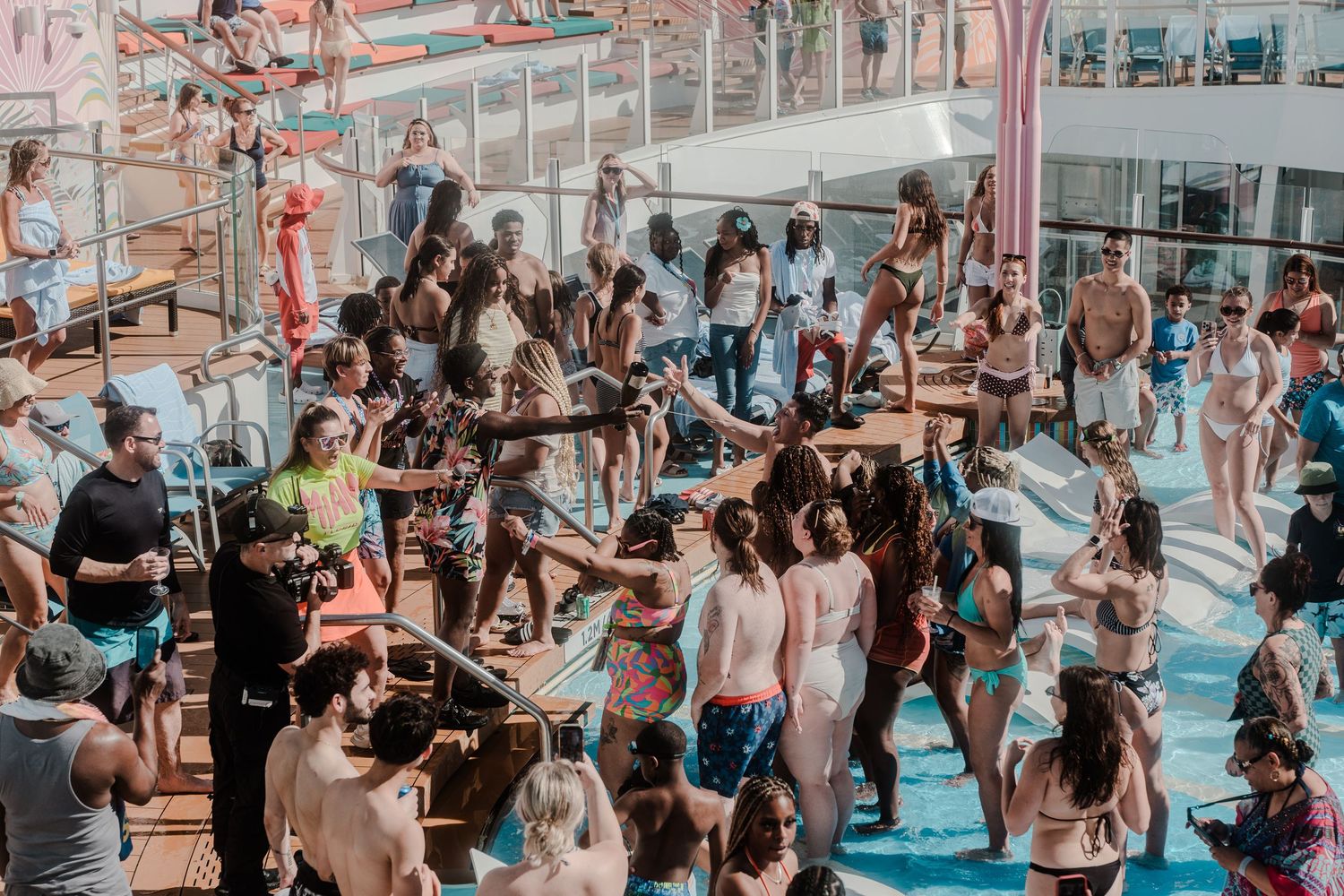 Large crowd of people in swimwear dancing and partying on a sunny cruise ship pool deck.