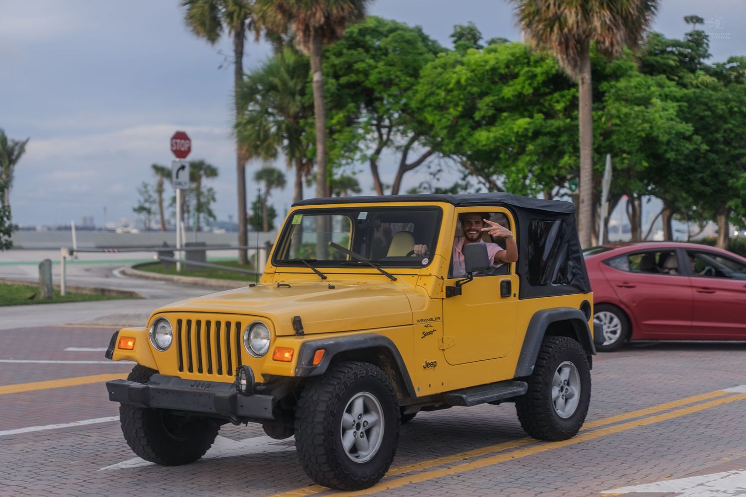 Yellow Jeep Wrangler driving on a sunny street in Key Biscayne, Florida with palm trees nearby.
