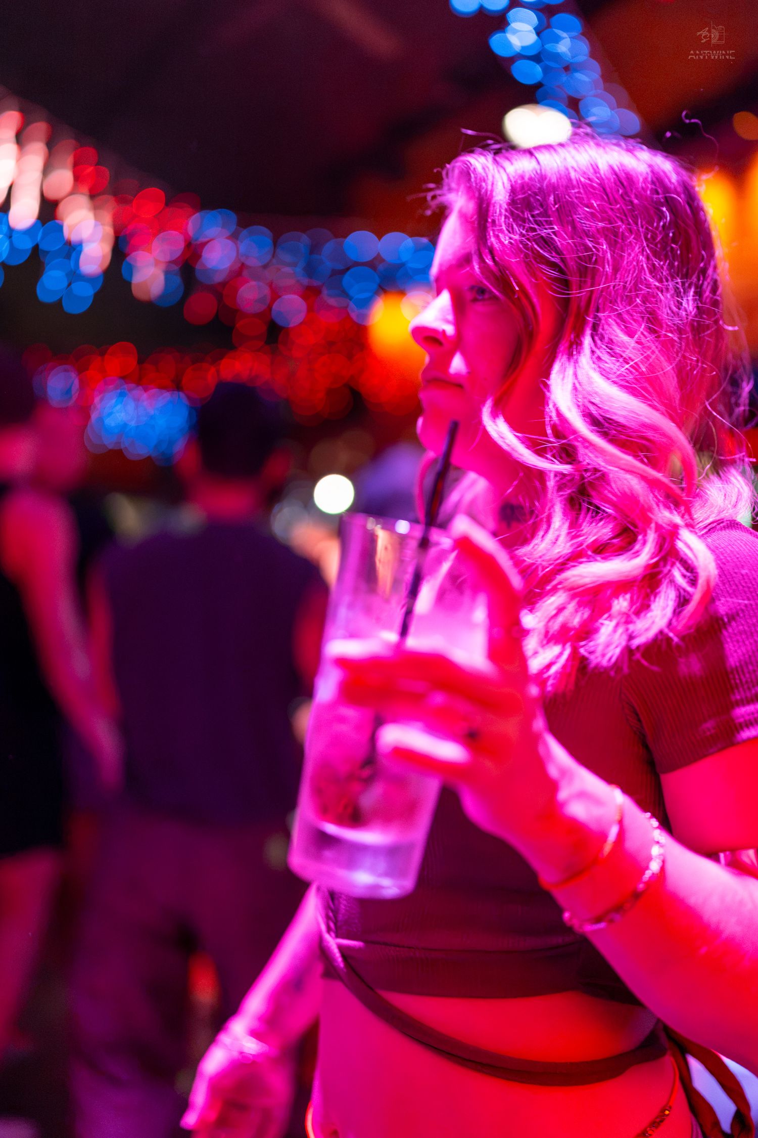 Woman holding cocktail drink in pink neon nightclub lighting with bokeh background.