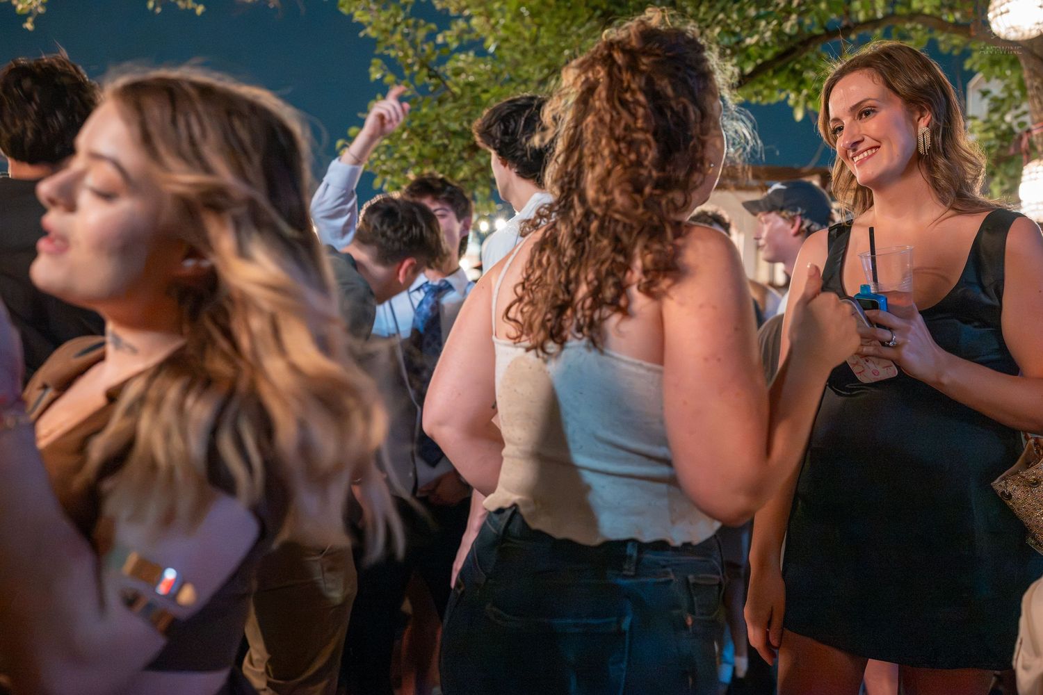 Young women dancing and socializing at an outdoor evening party, smiling and holding drinks.