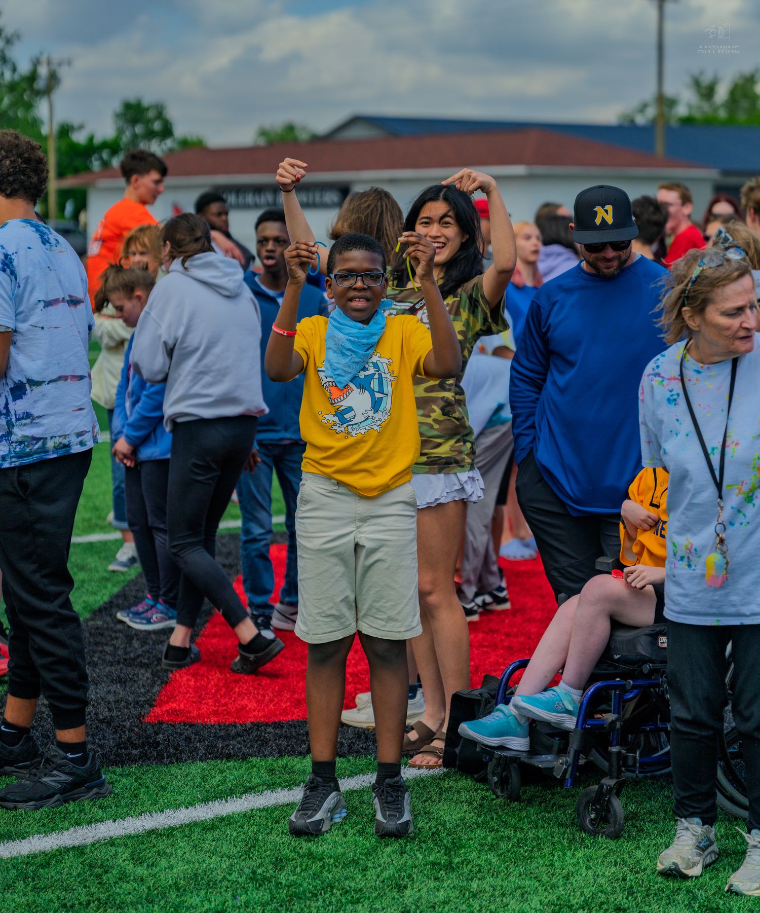 Excited child in yellow shirt celebrates with arms raised at an outdoor school sports event on a green field.