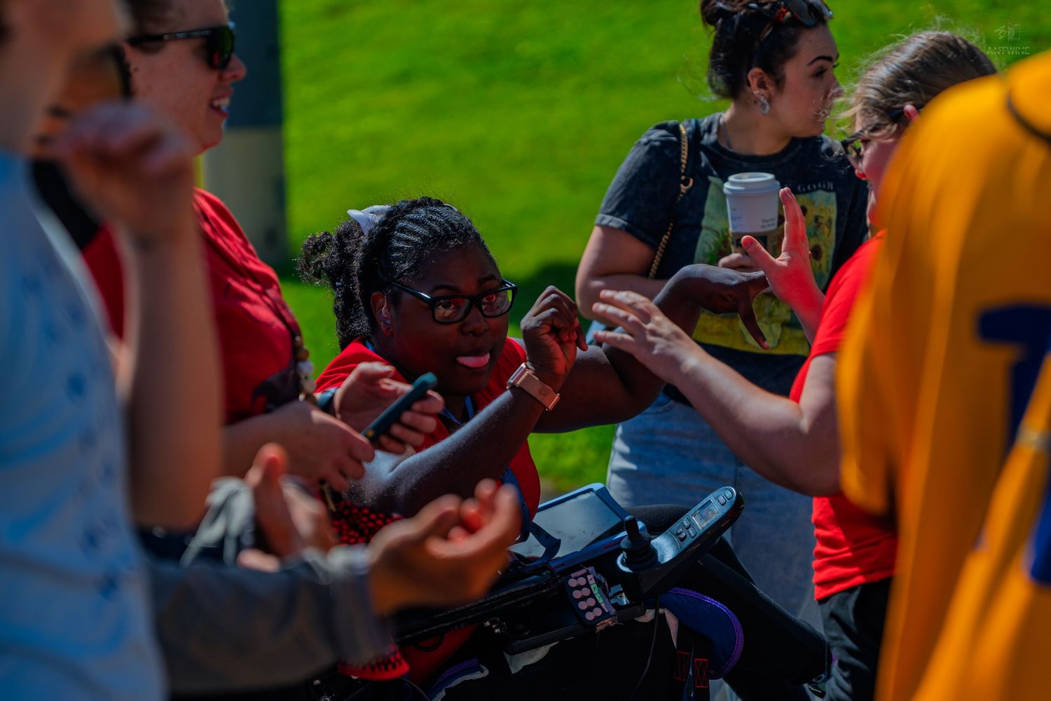 Young athletes gather outdoors, exchanging items and socializing during a sunny sports event.