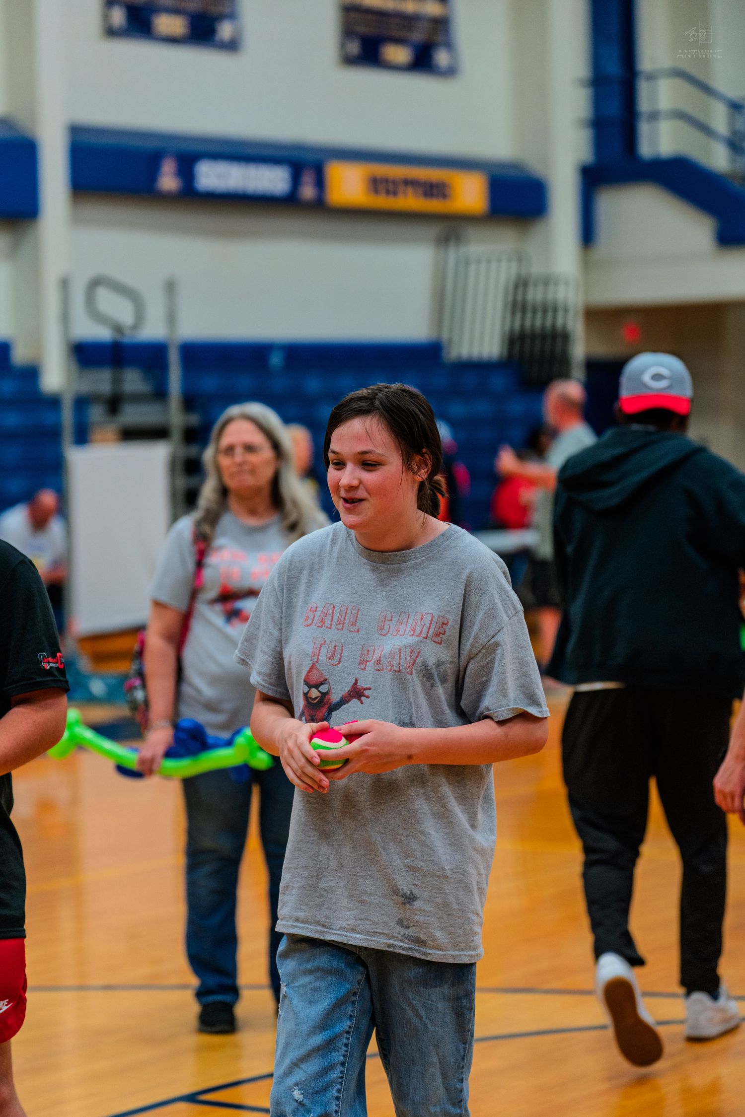 Young woman in gray t-shirt holding a ball on a gymnasium court during an indoor sports event.