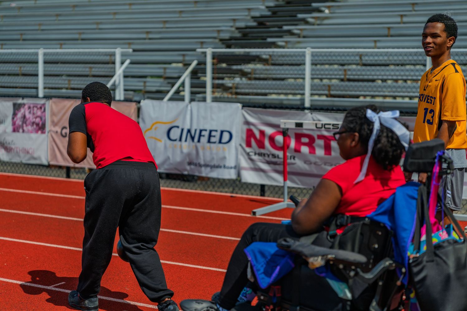 Athletes at a wheelchair track event on a red running track with Cinfed Norte sponsorship banner in background.