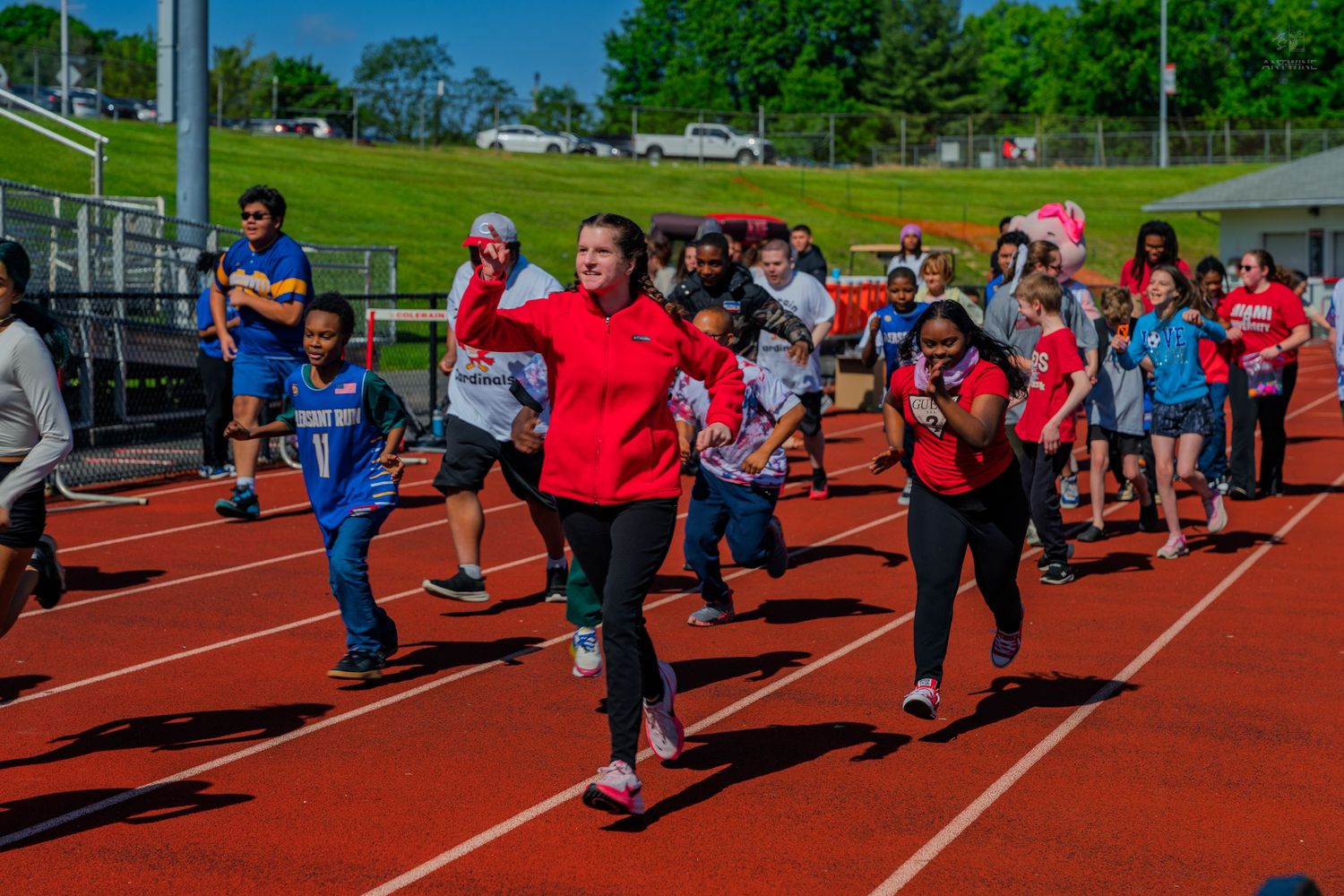 Students running on a red track during an outdoor school field day event on a sunny spring day.