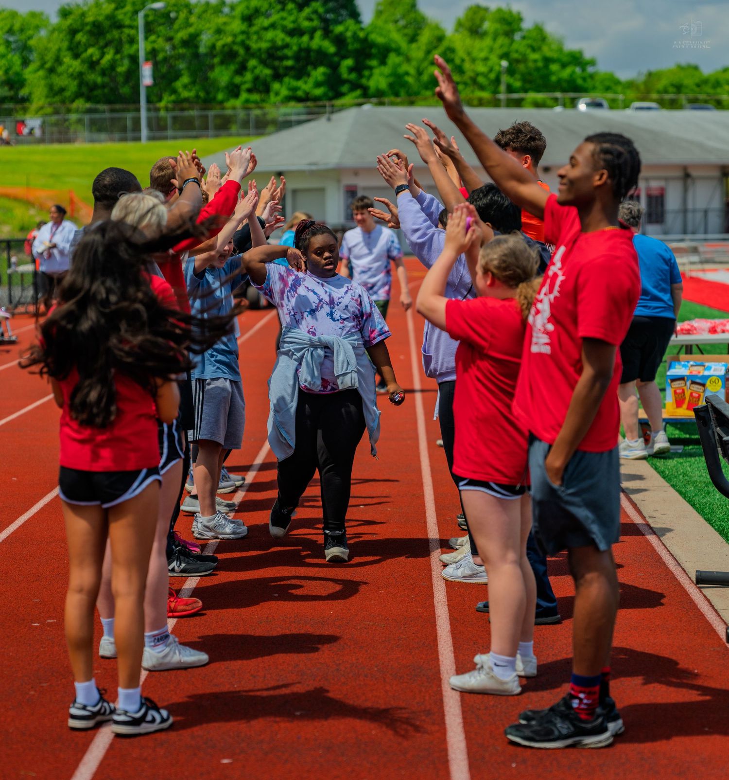 Students forming a high-five tunnel on a red track during an outdoor school sports event on a sunny day.