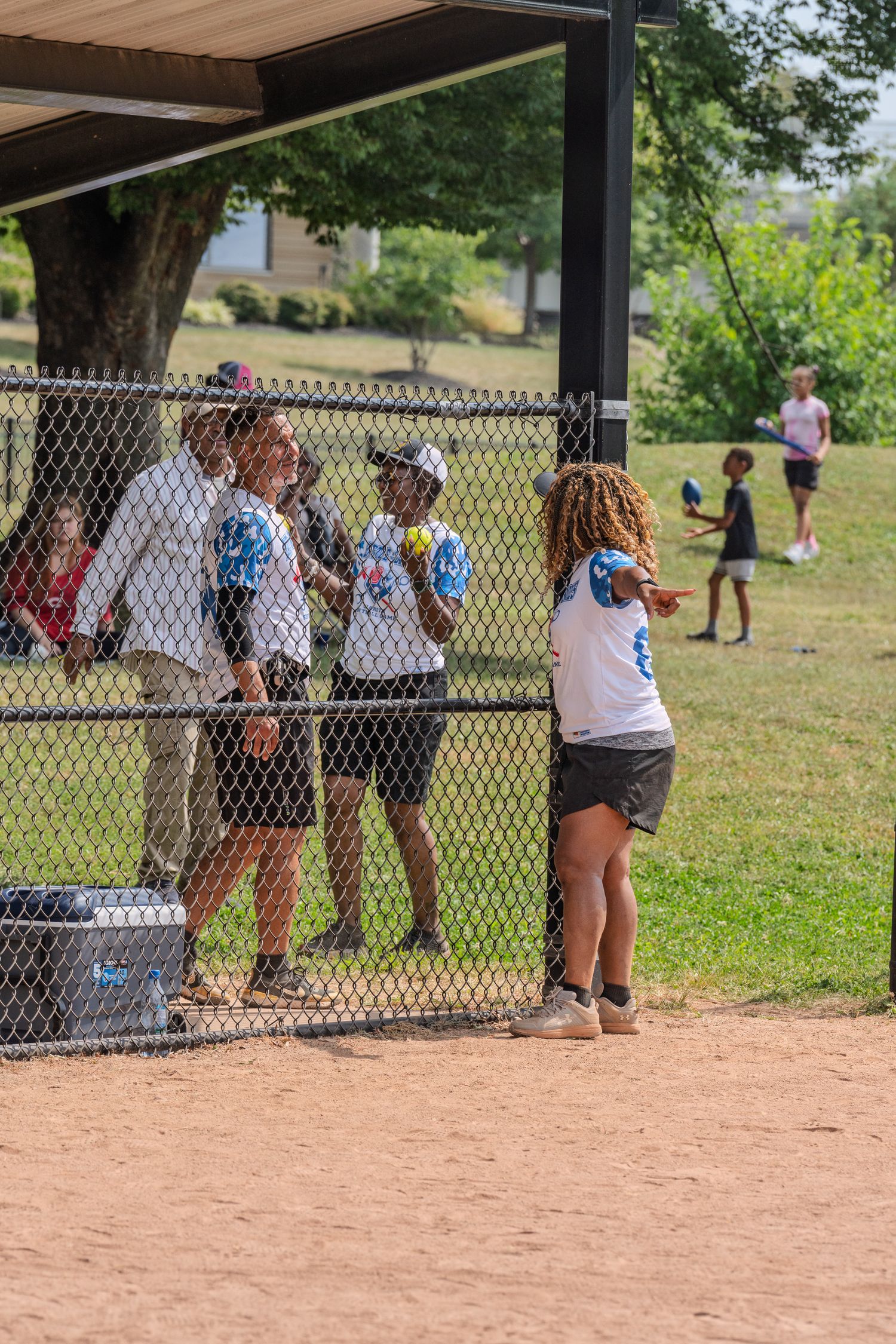Softball players in EOP uniforms watch the game from behind a chain-link dugout fence.