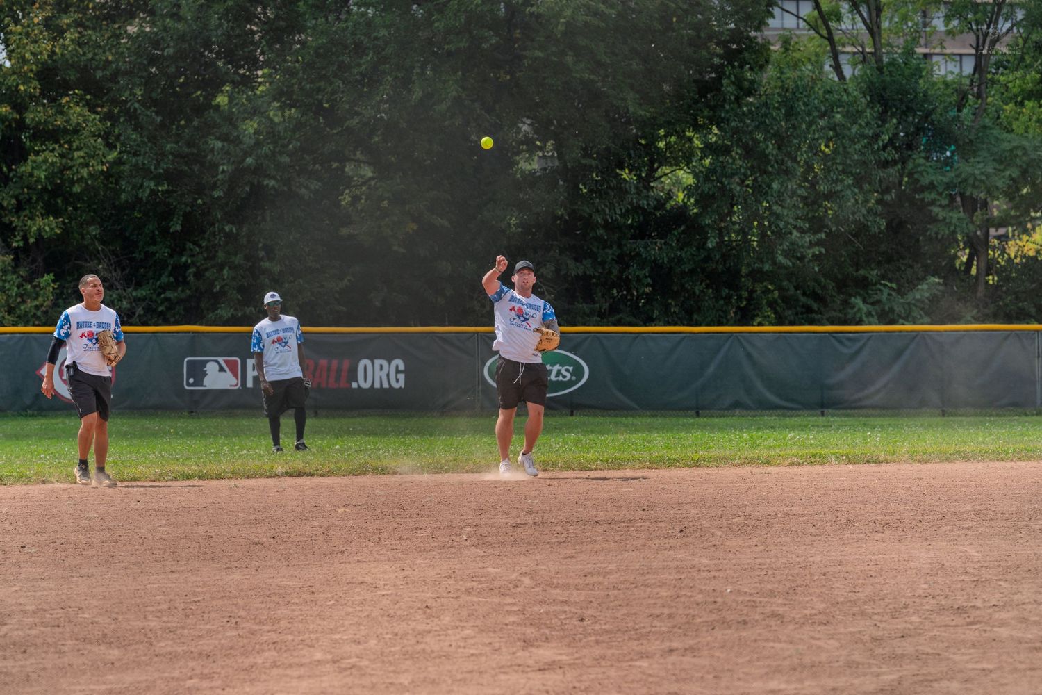 Softball players on a dirt field with one player throwing the ball during an outdoor game.