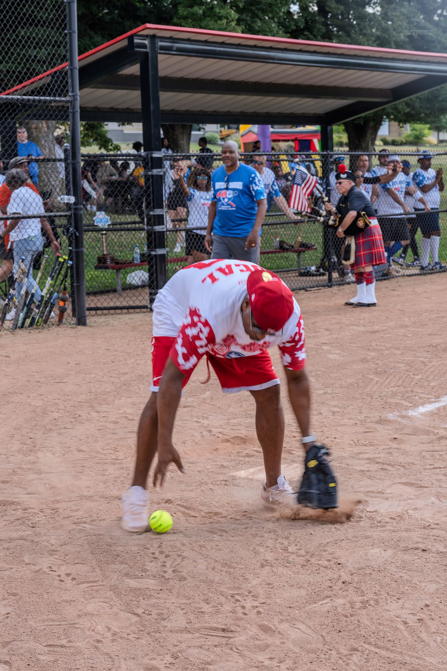 Softball player in red and white uniform fielding a ground ball during an outdoor recreational game.