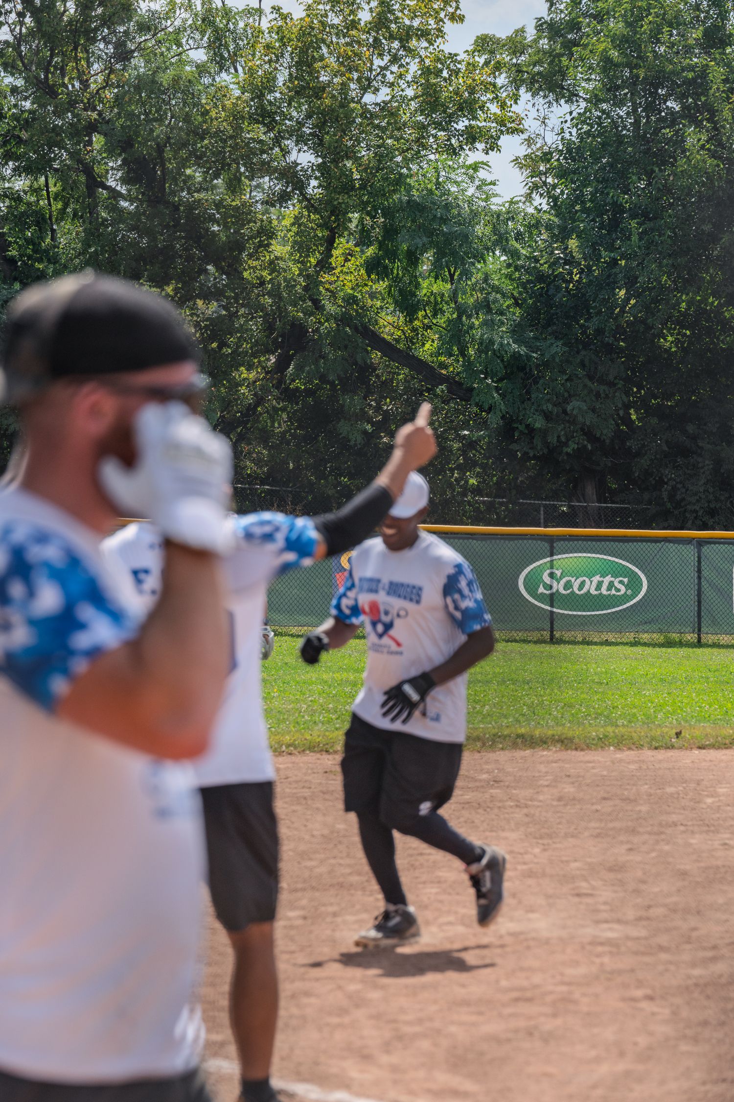Baseball player giving thumbs up while running bases during a charity softball game outdoors.