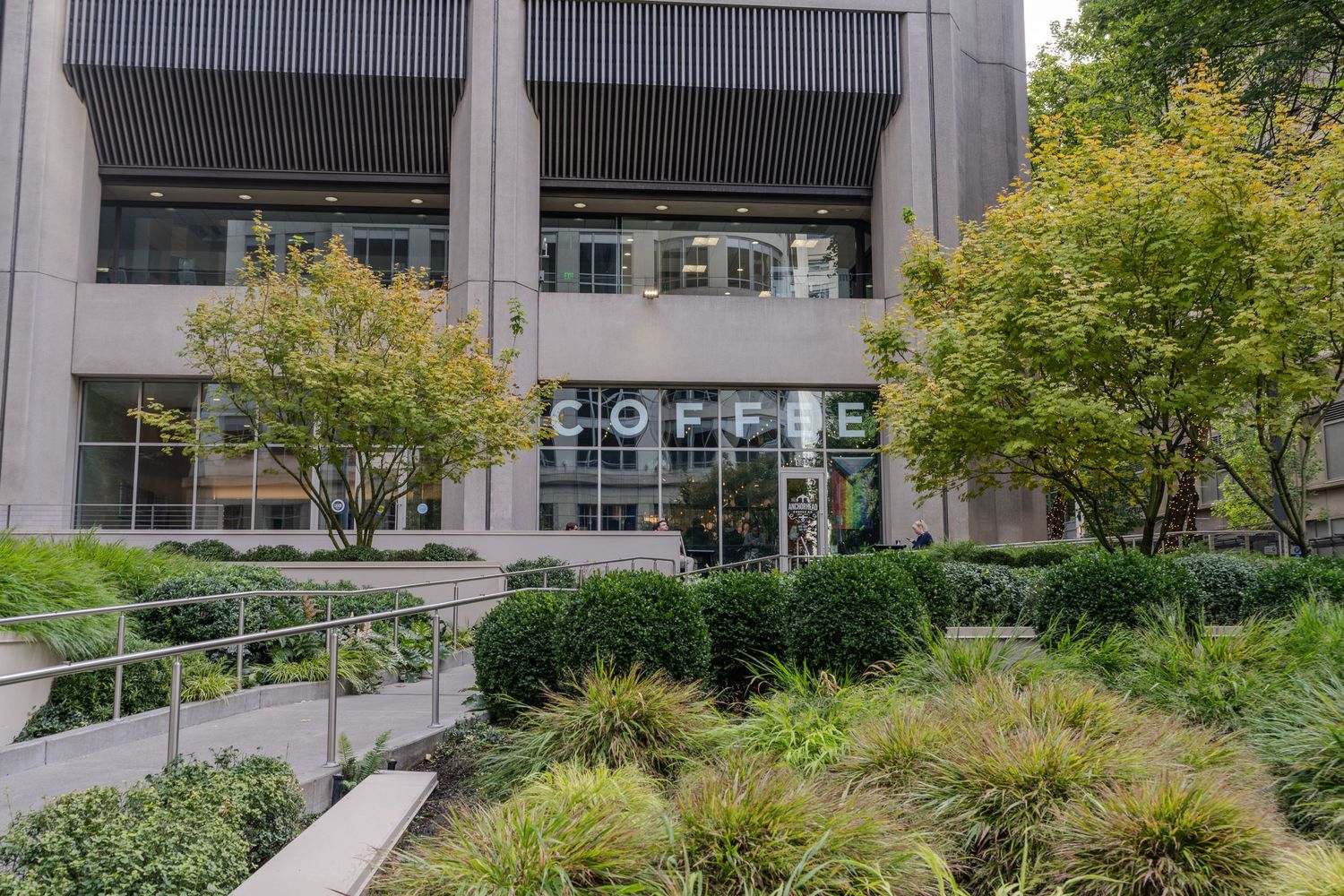 Modern office building exterior with lush green landscaping and Coffee shop signage.