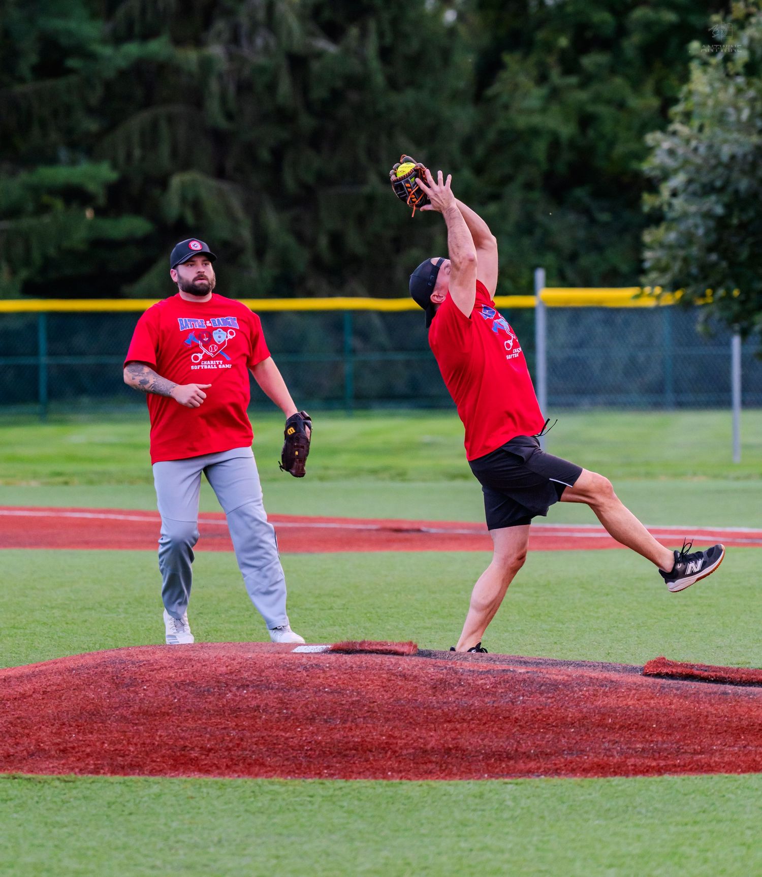 Two baseball players in red uniforms, one catching a fly ball on the pitcher's mound during a game.